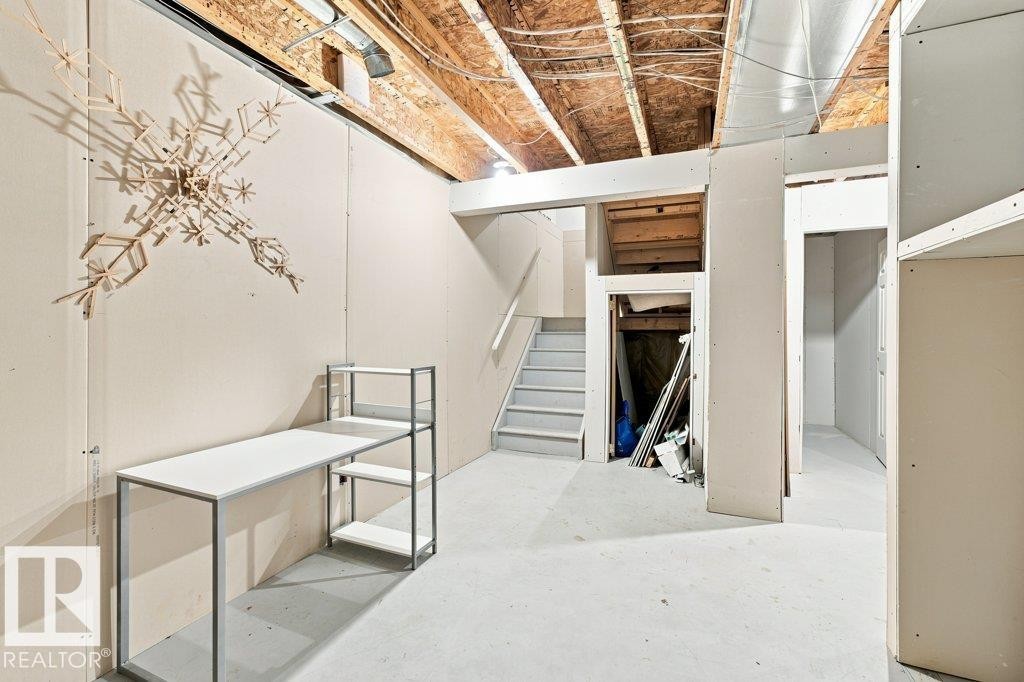 Unfinished basement featuring exposed ceiling joists and ductwork, gypsum board walls, concrete flooring, and a stairway with painted treads - 2811 33 Street, Edmonton, AB