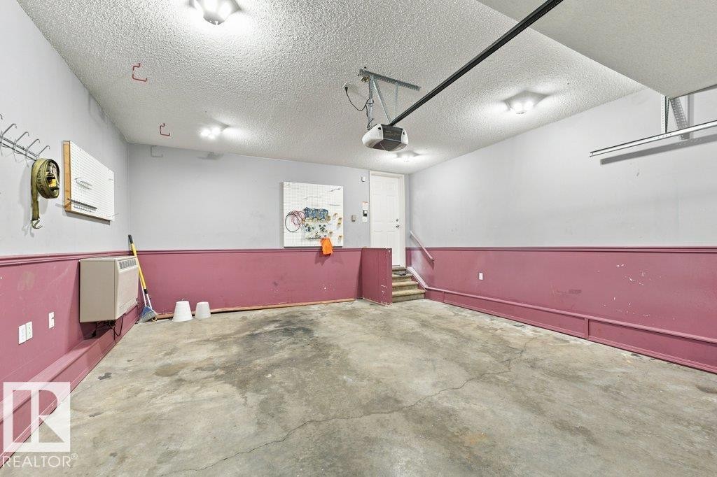 Spacious garage featuring a concrete floor, built-in overhead lighting, and interior access via a white door and small staircase - 2811 33 Street, Edmonton, AB