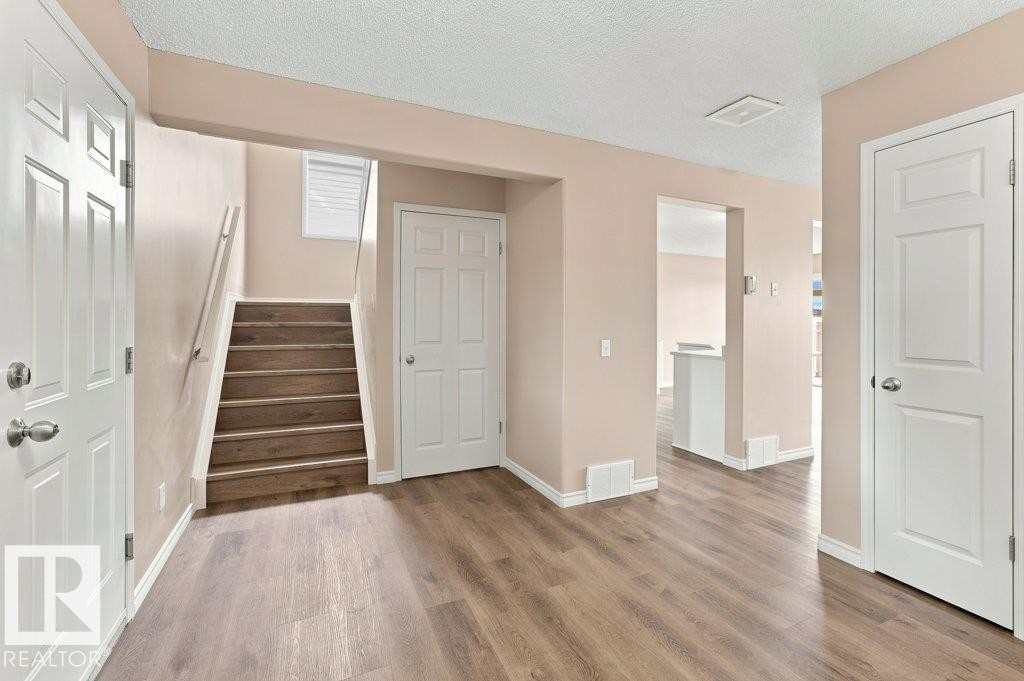 Entryway featuring wood-finish flooring, light peach walls, white trim, and a staircase with a white handrail - 2811 33 Street, Edmonton, AB