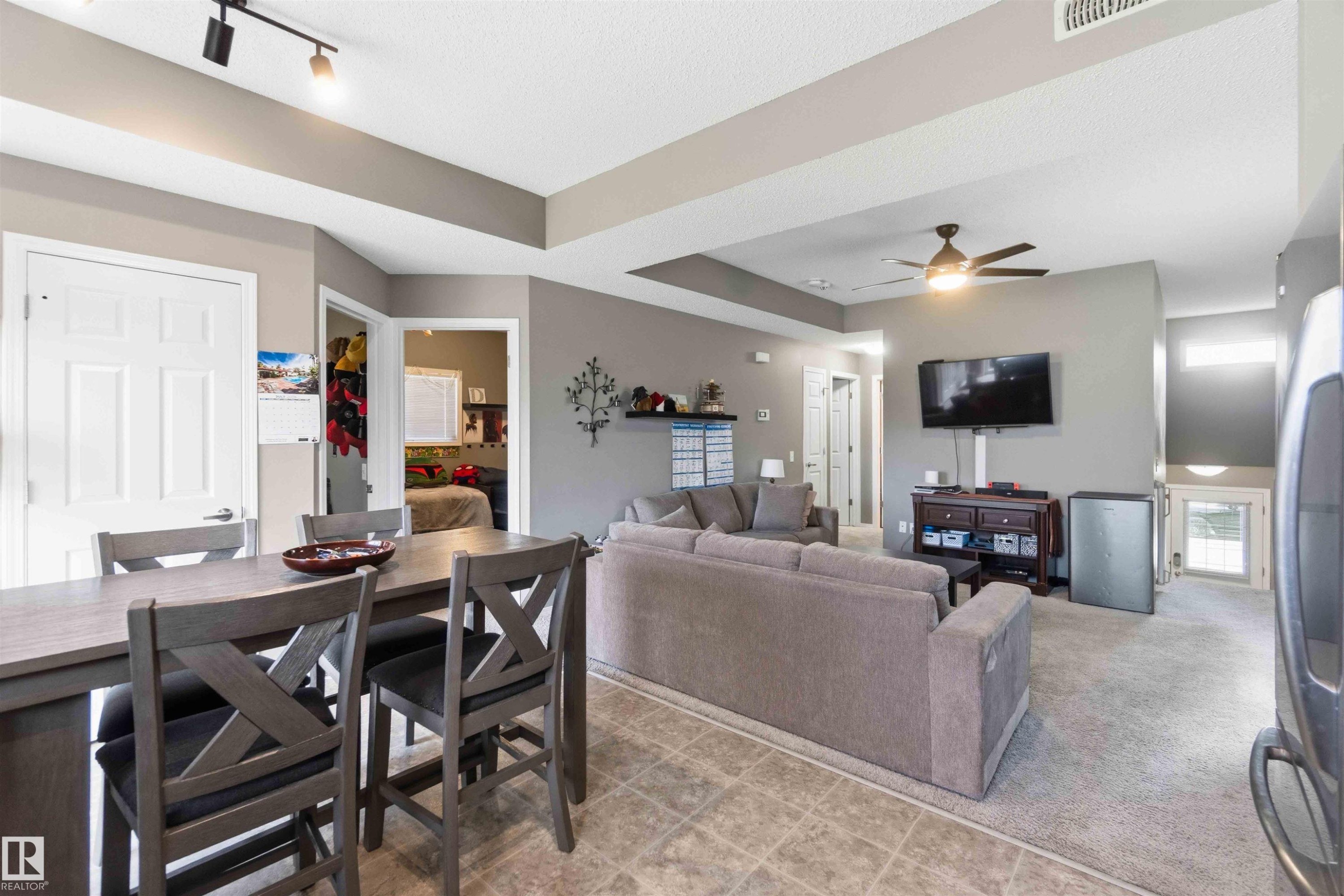 Open-concept interior featuring a breakfast bar, track lighting, ceiling fan, and mixed flooring with tile and carpet - 24 6520 2 Avenue, Edmonton, AB