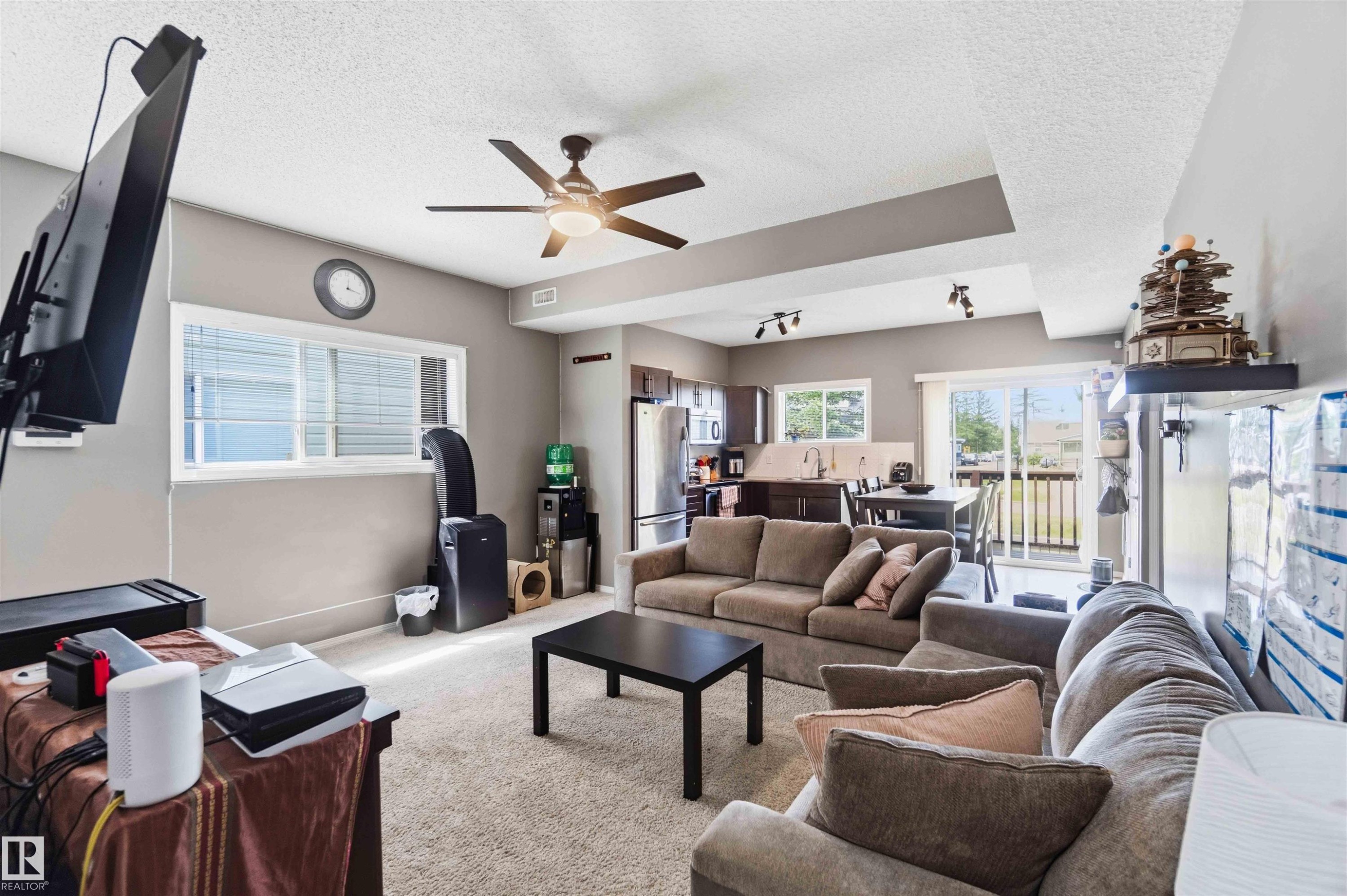 Open-concept living area featuring neutral carpeting, a ceiling fan with integrated lighting, and recessed ceiling details - 24 6520 2 Avenue, Edmonton, AB