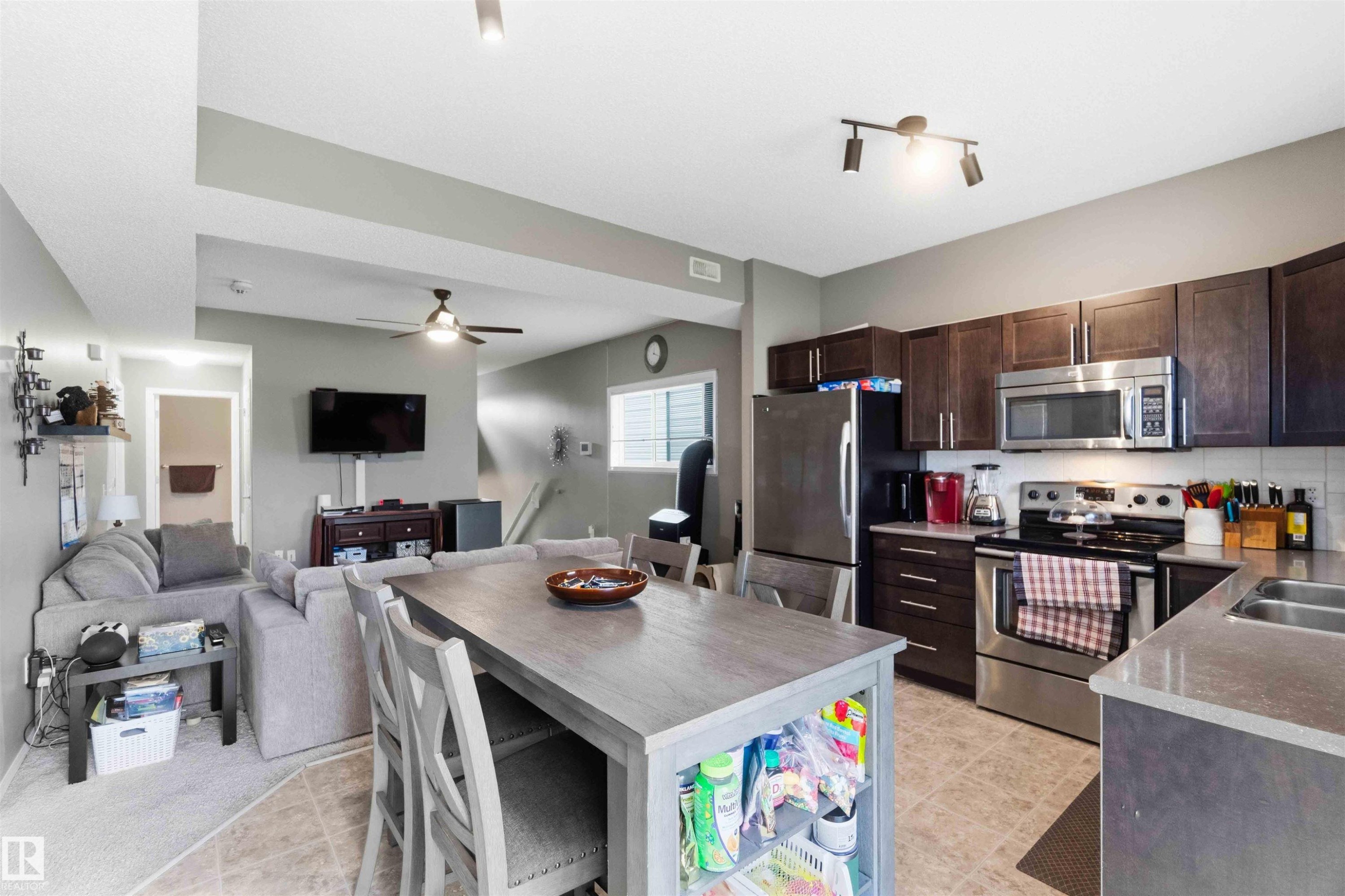 Open-concept kitchen and living area featuring wood-finish cabinetry, stainless steel appliances, a light-toned countertop, and a ceiling fan - 24 6520 2 Avenue, Edmonton, AB