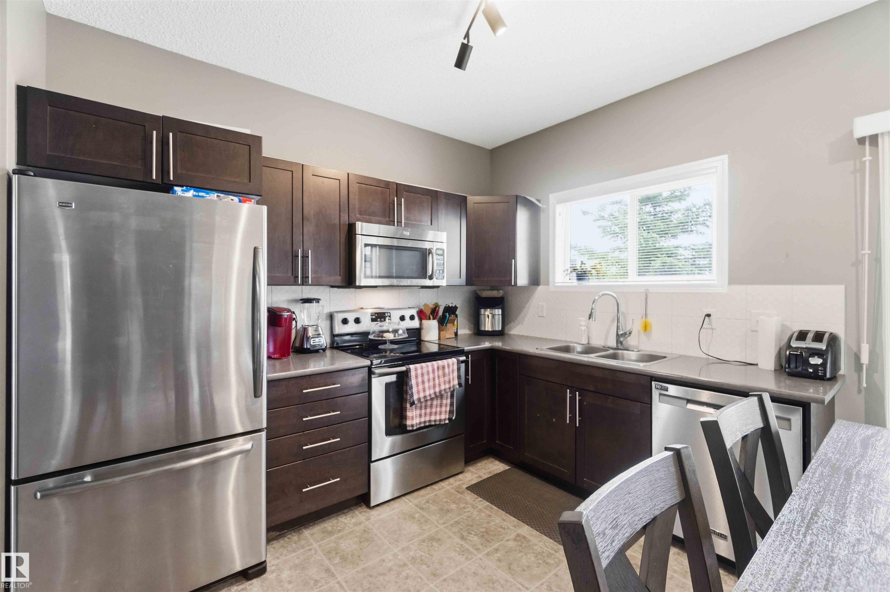 Modern kitchen featuring dark wood-finish cabinetry, stainless steel appliances, and ample counter space - 24 6520 2 Avenue, Edmonton, AB