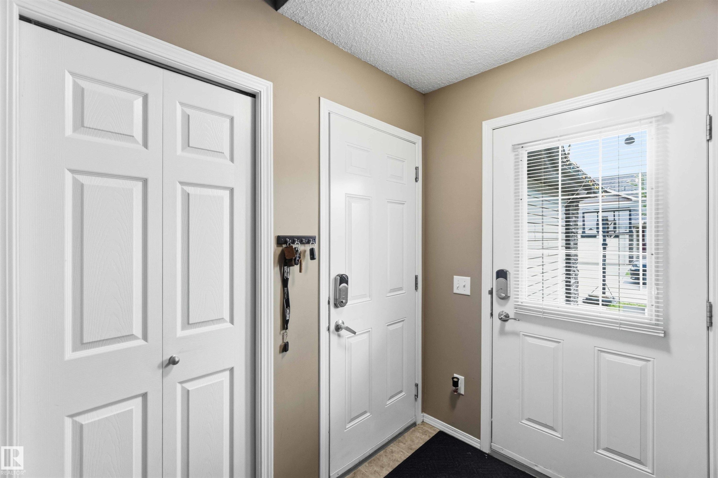 Entryway featuring a paneled door with an integrated window and blinds, light tan walls, and a textured ceiling - 24 6520 2 Avenue, Edmonton, AB