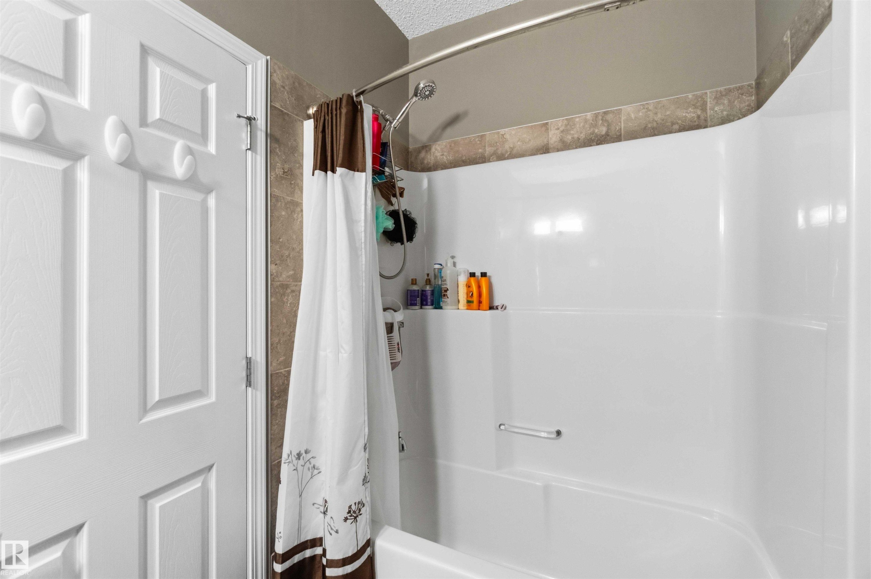 White fiberglass tub and shower combination with a curved basin and integrated shelving - 24 6520 2 Avenue, Edmonton, AB