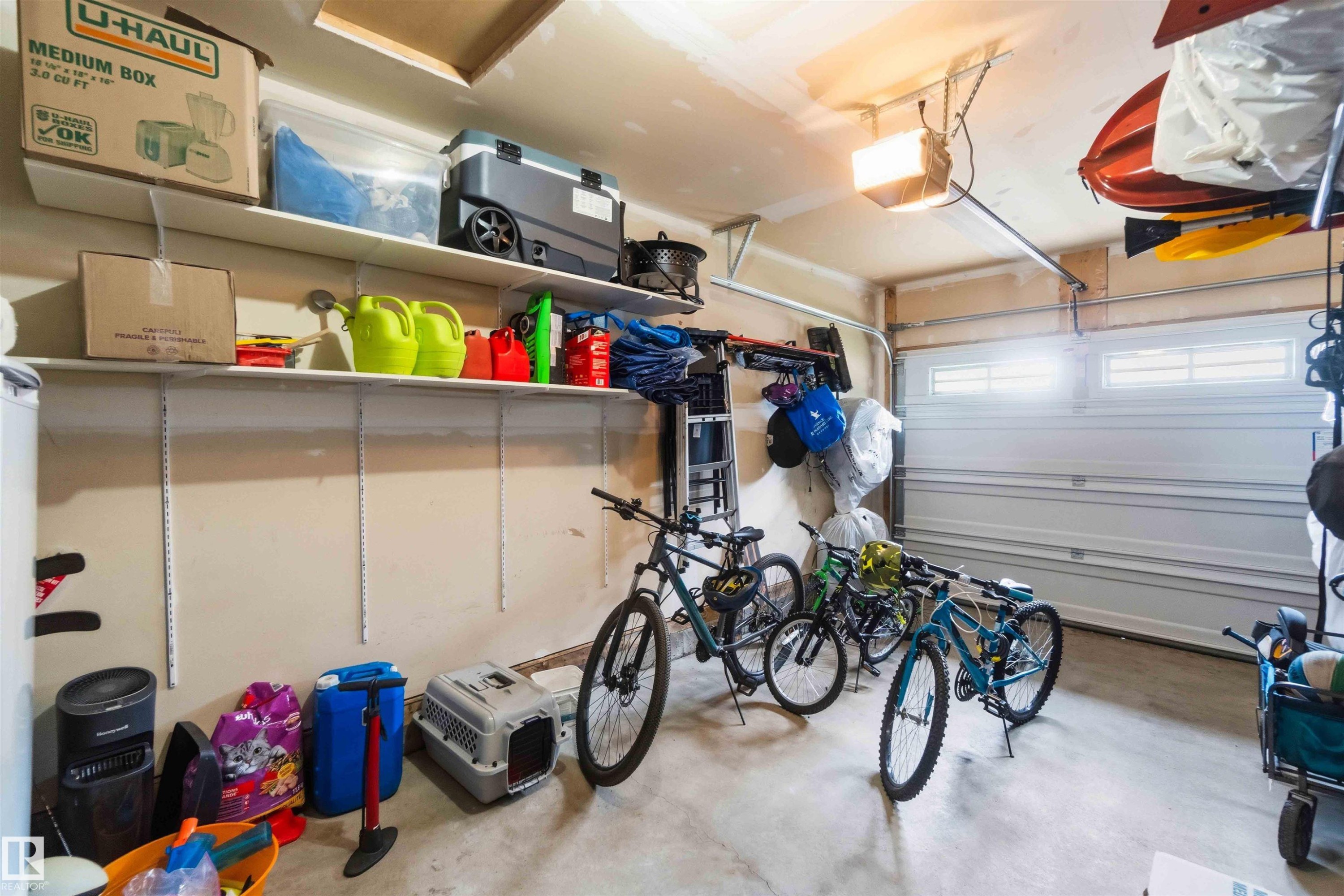 Attached garage featuring a white overhead door with upper window panels, overhead lighting, and built-in wall shelving - 24 6520 2 Avenue, Edmonton, AB