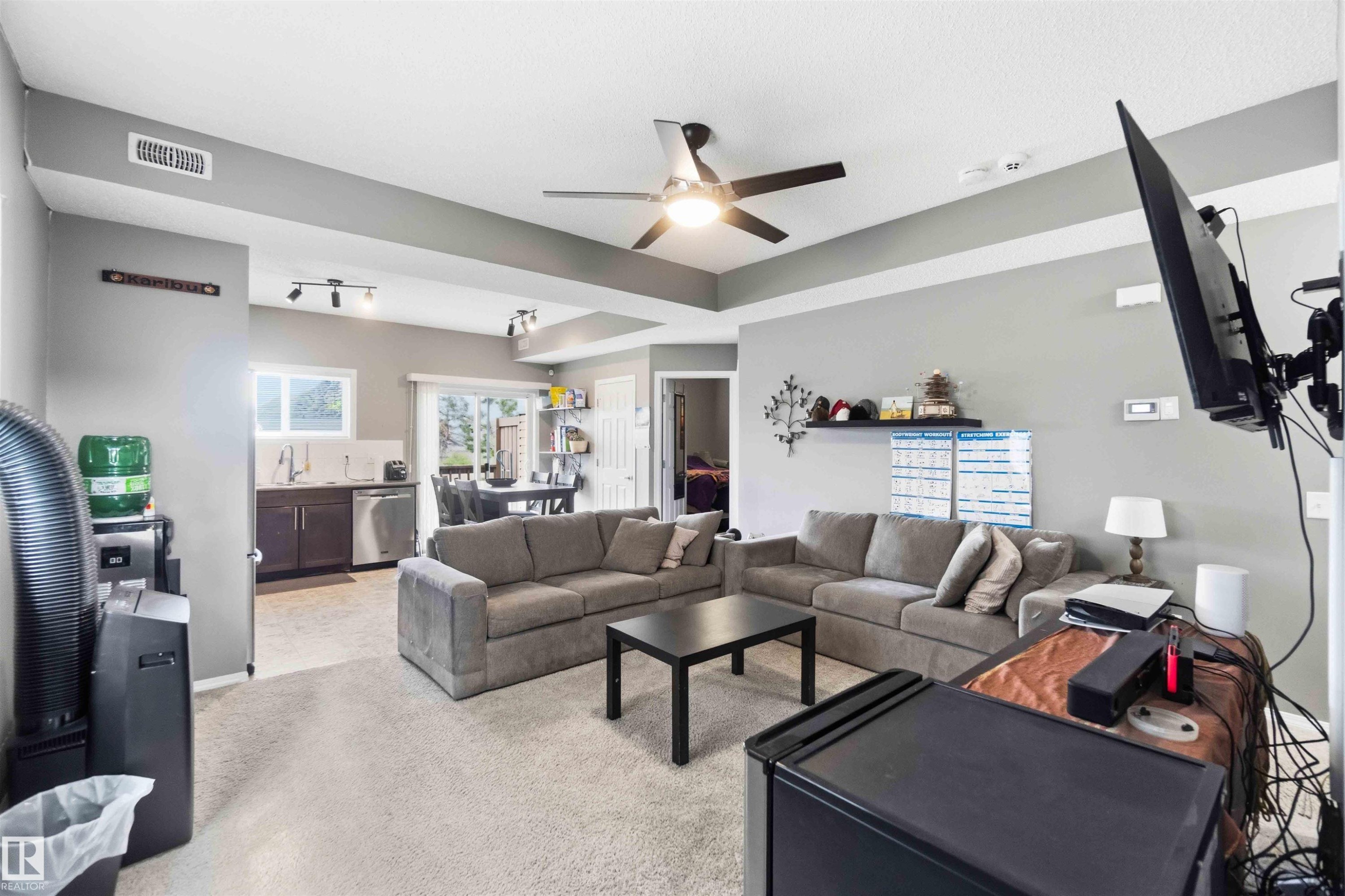Open-concept living space featuring a ceiling fan with integrated lighting, wood-finish flooring in the kitchen area, and a sliding glass door - 24 6520 2 Avenue, Edmonton, AB