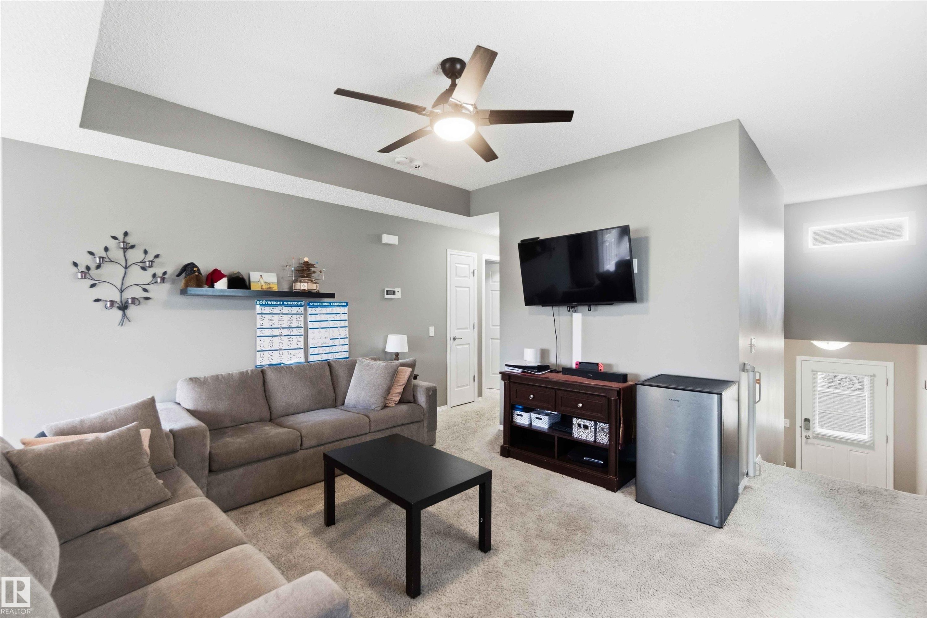 Spacious living area featuring neutral carpeting, a ceiling fan with integrated lighting, and recessed ceiling details - 24 6520 2 Avenue, Edmonton, AB
