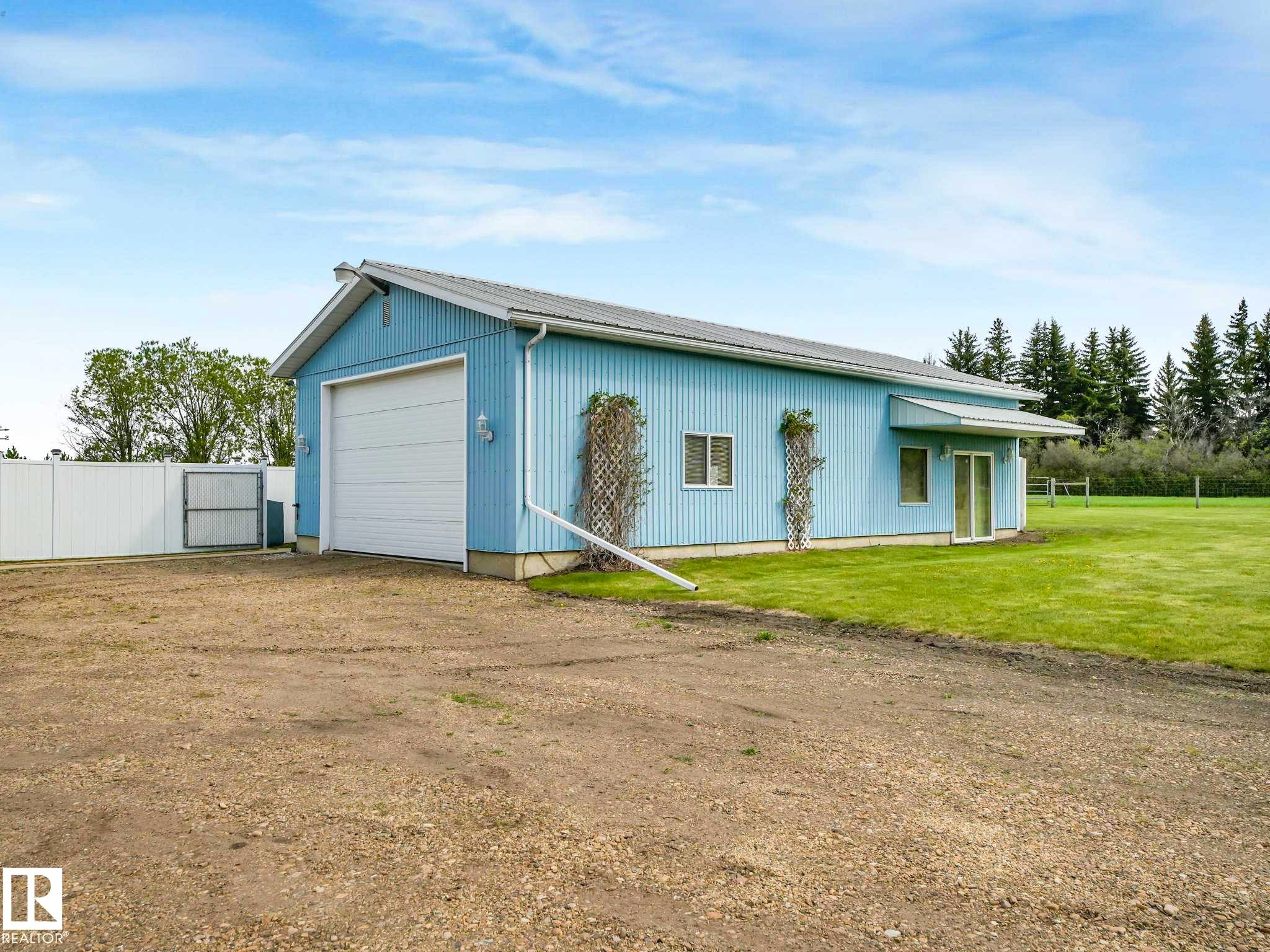 Light blue corrugated metal building featuring a large white garage door, two rectangular windows, and a sliding glass entry door - 53133 Rge Road 223, Rural Strathcona County, AB - Outdoor