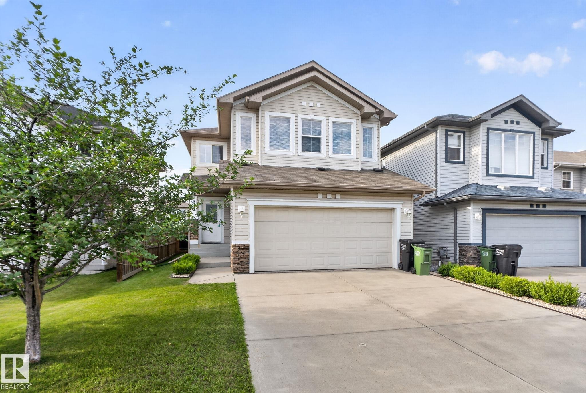 Two-story residential exterior featuring light-colored siding, a two-car attached garage, stone accents, and a concrete driveway - 7858 170A Avenue, Edmonton, AB