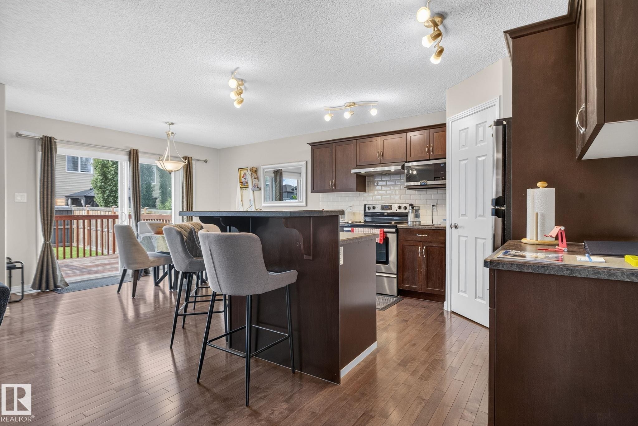 Open-concept kitchen and dining area featuring rich wood-finish flooring, dark wood cabinetry, and stainless steel appliances - 7858 170A Avenue, Edmonton, AB