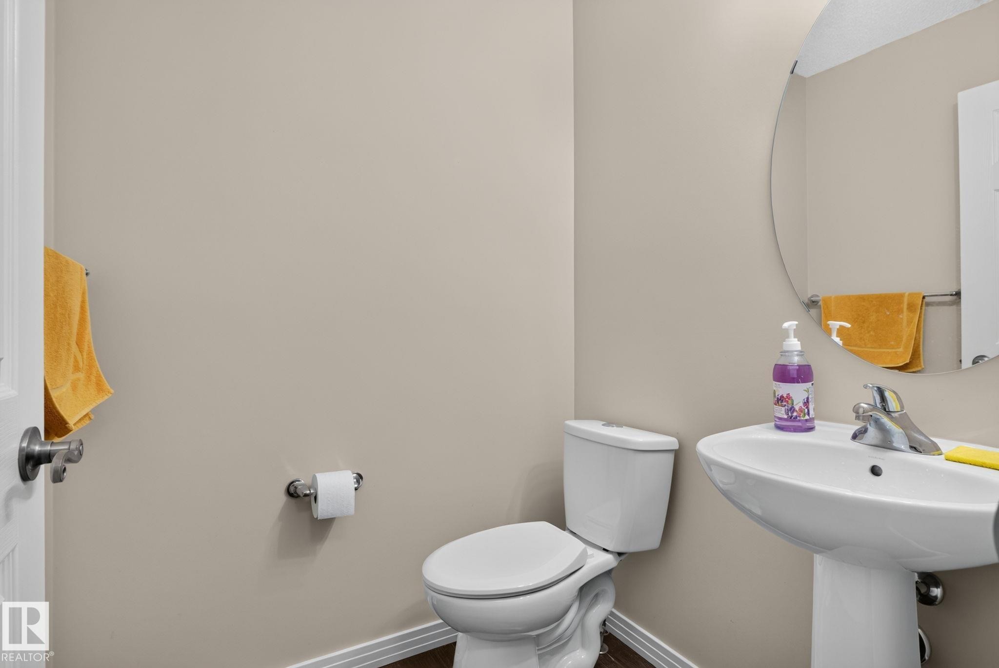 Powder room featuring a pedestal sink with chrome faucet, a standard toilet, and wood-finish flooring - 7858 170A Avenue, Edmonton, AB