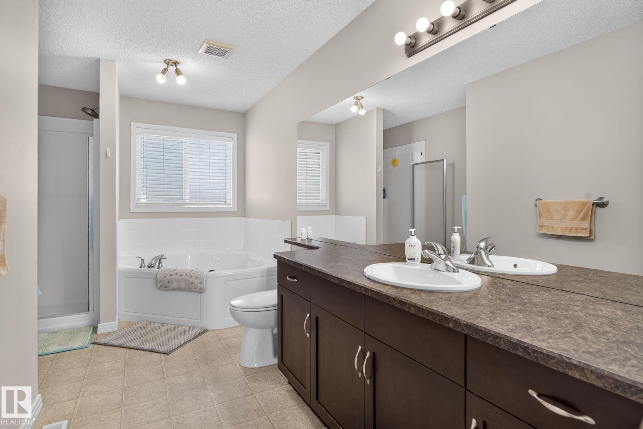 Expansive bathroom featuring a dual vanity with integrated sinks, a wide mirror, and a full-size bathtub - 7858 170A Avenue, Edmonton, AB