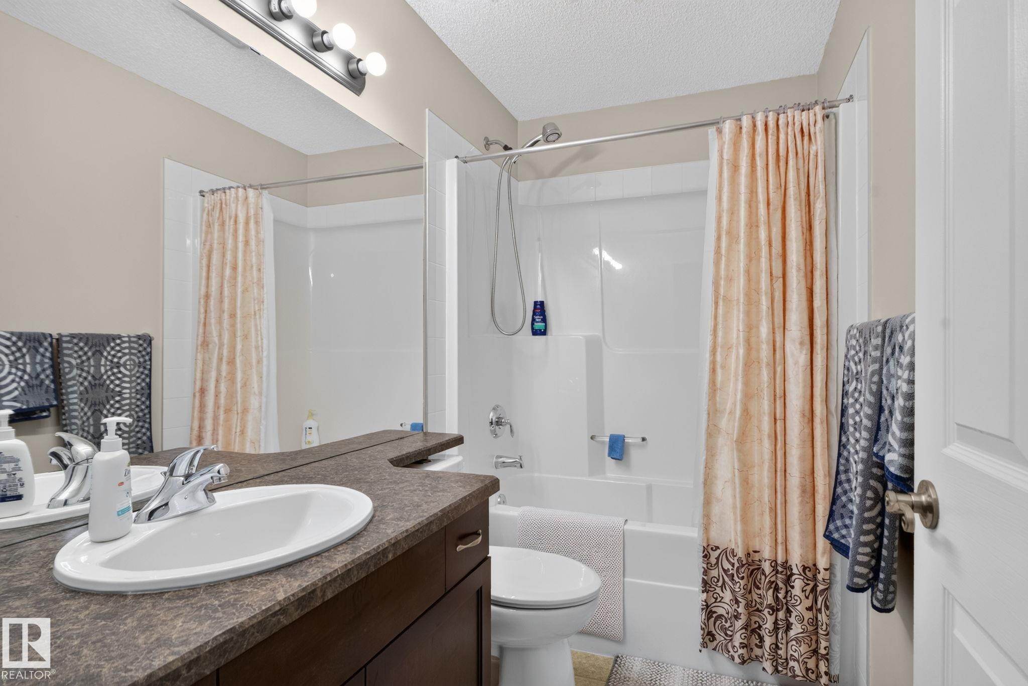 Bathroom featuring a dark wood vanity with an integrated oval sink, a speckled countertop, and a vanity mirror - 7858 170A Avenue, Edmonton, AB