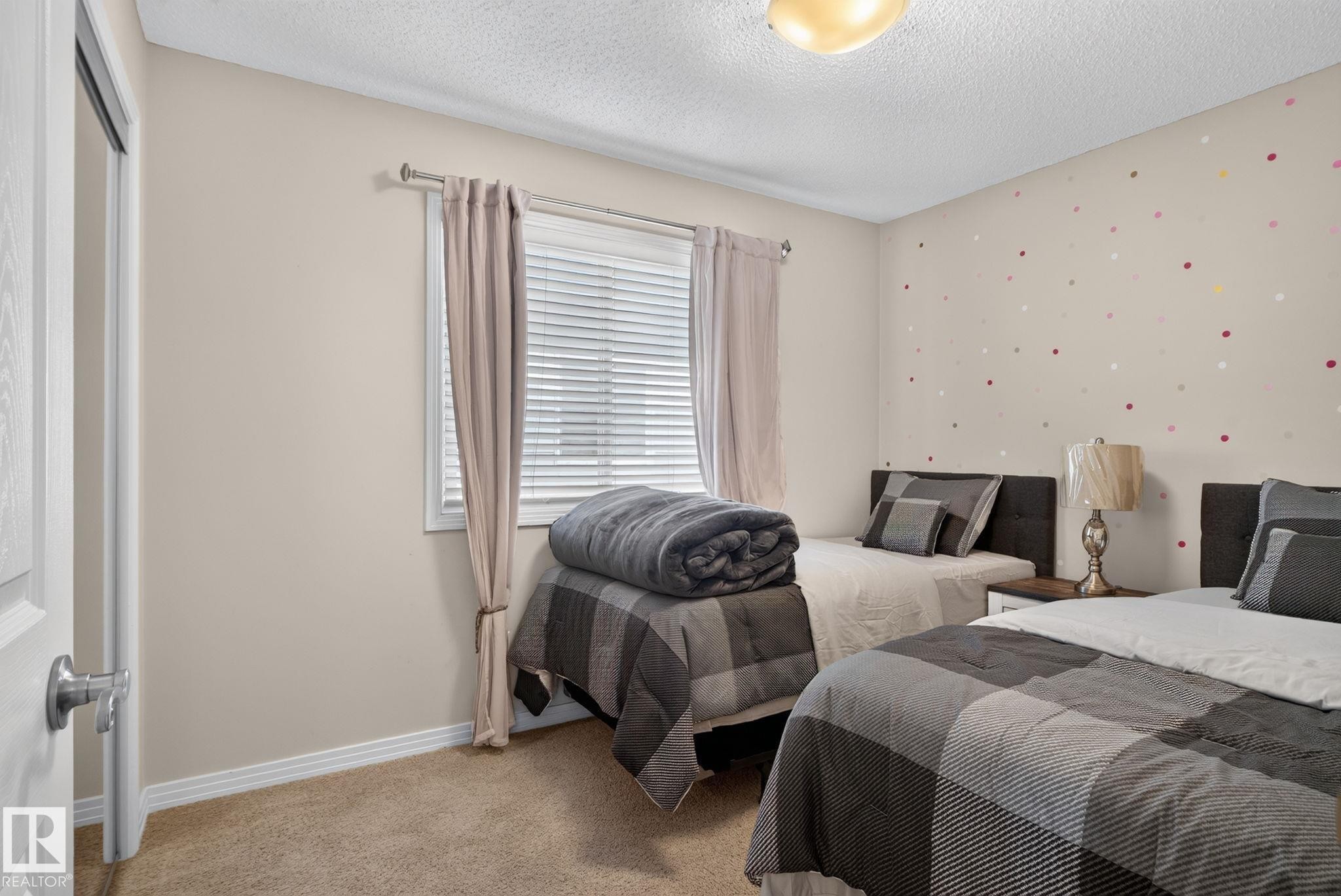 Carpeted room with a textured ceiling and a window featuring blinds and drapes - 7858 170A Avenue, Edmonton, AB