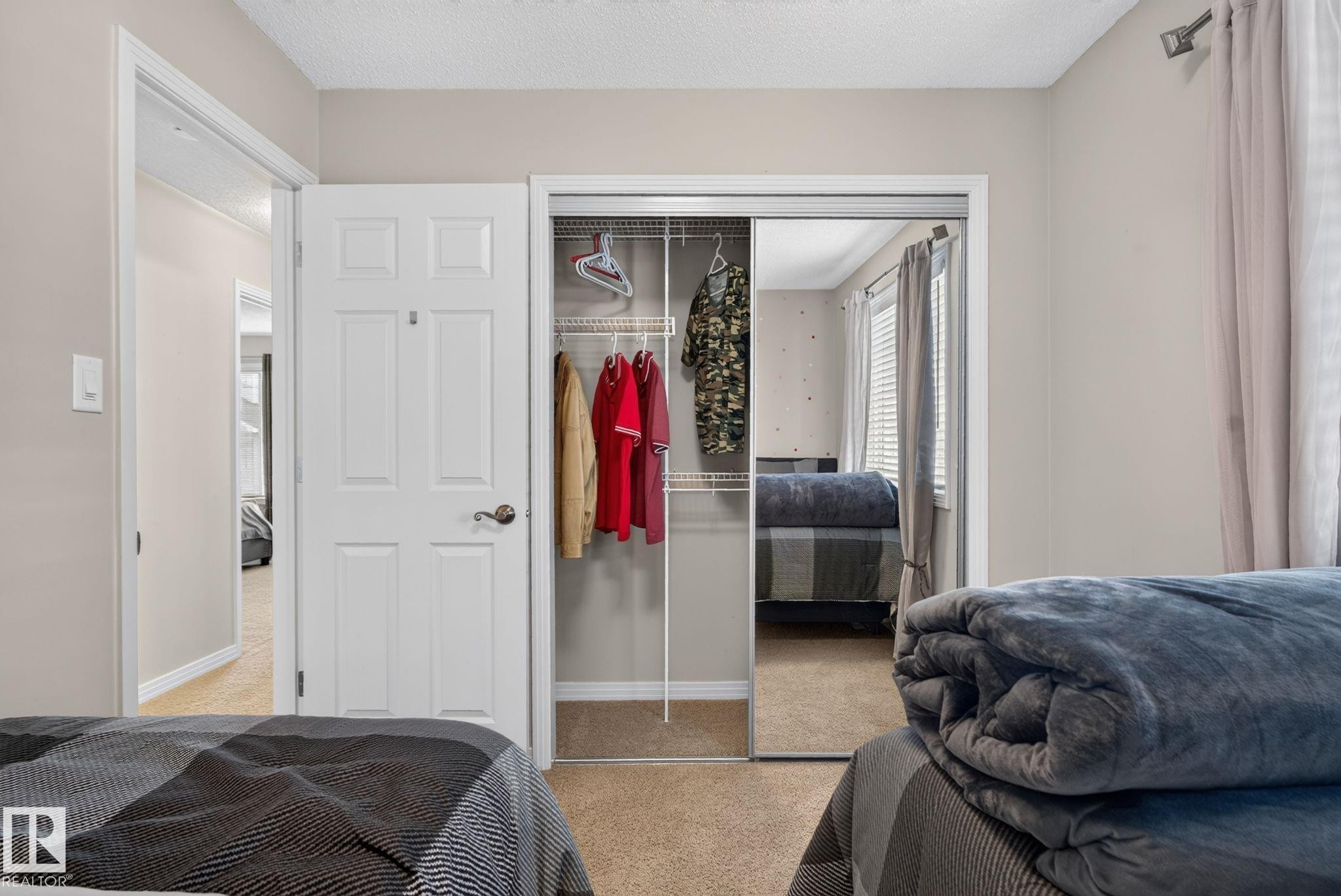 Bedroom featuring carpeting, a white panel door, and mirrored closet doors with wire shelving - 7858 170A Avenue, Edmonton, AB
