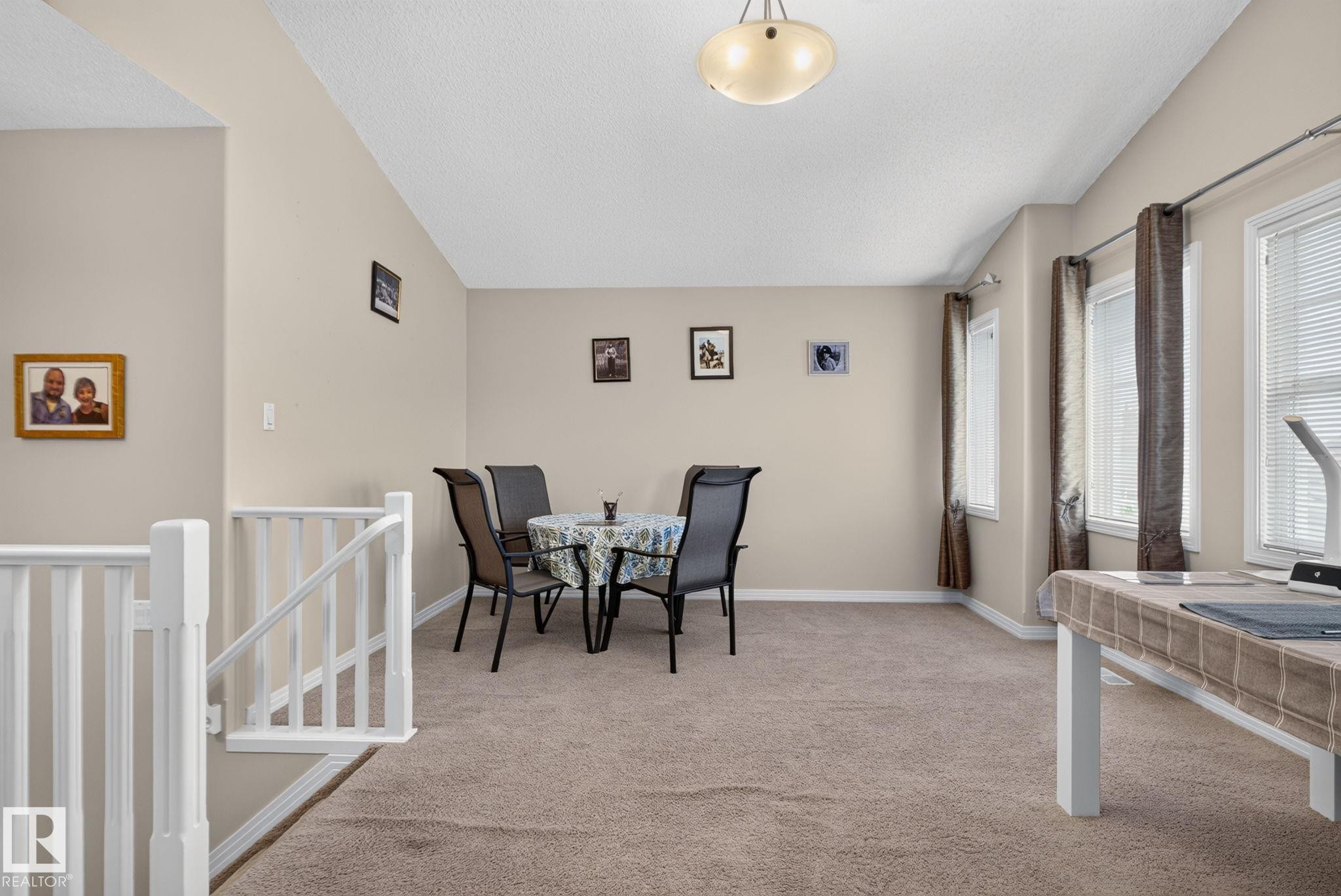 Carpeted upper-level landing featuring a white railing, a vaulted ceiling, and multiple windows - 7858 170A Avenue, Edmonton, AB