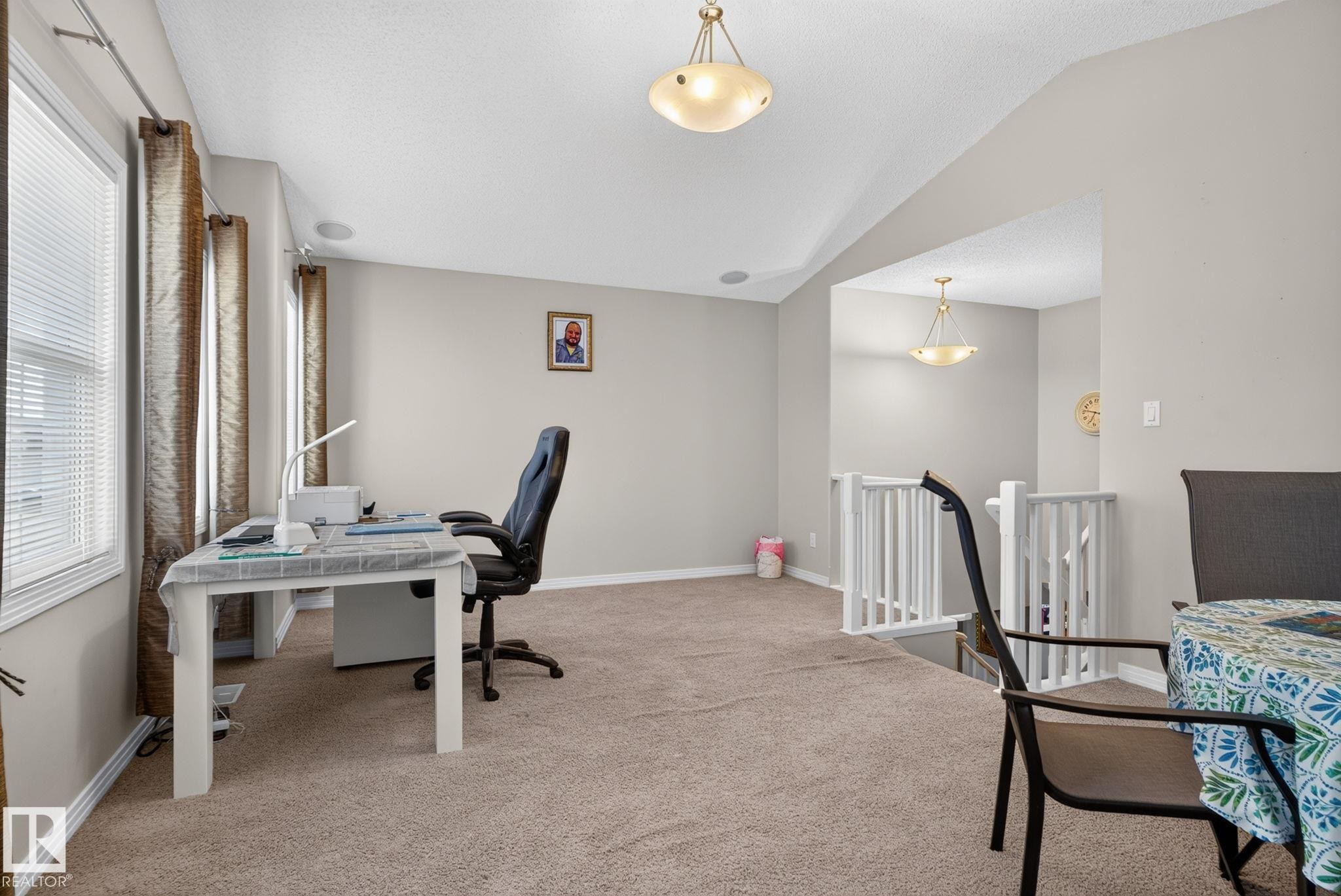 Carpeted upper-level space featuring a white painted railing, multiple windows with blinds, and ceiling-mounted light fixtures - 7858 170A Avenue, Edmonton, AB