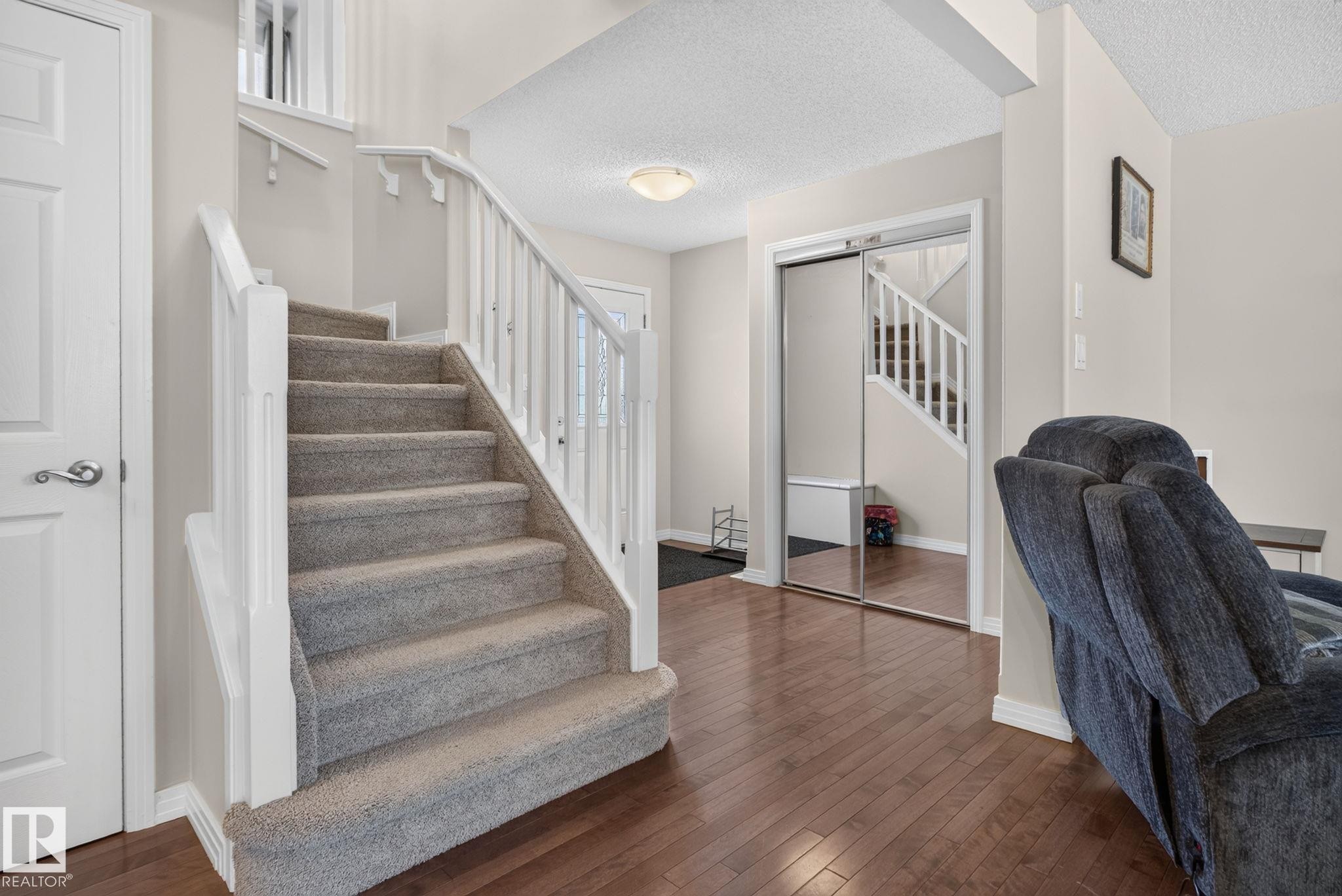 Carpeted staircase with white balusters and handrails, complemented by wood-finish flooring - 7858 170A Avenue, Edmonton, AB
