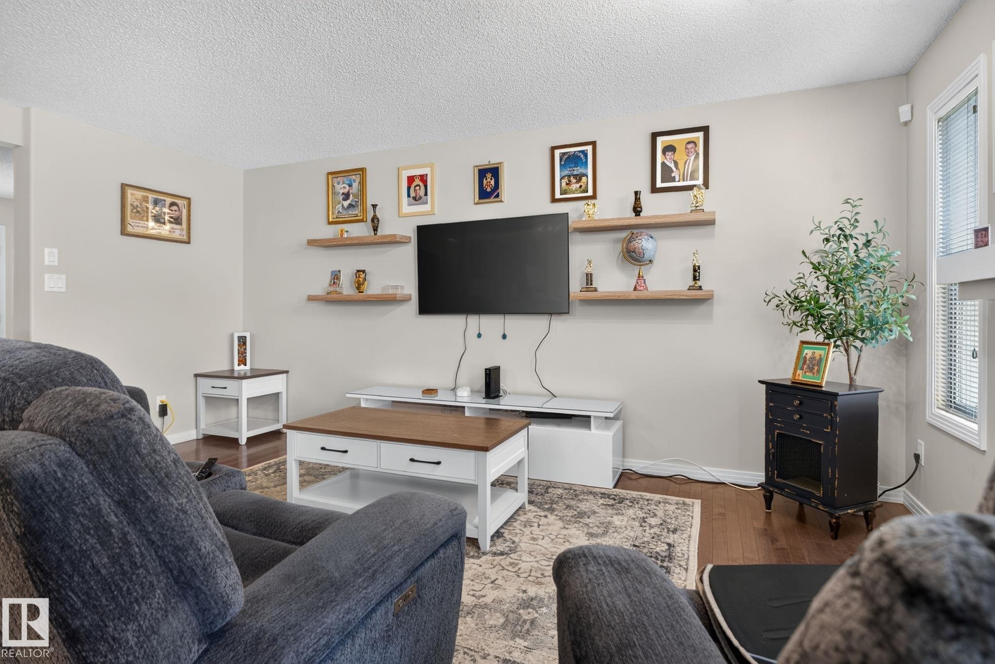 Living area featuring wood-finish flooring, light-toned walls, and a window with blinds - 7858 170A Avenue, Edmonton, AB