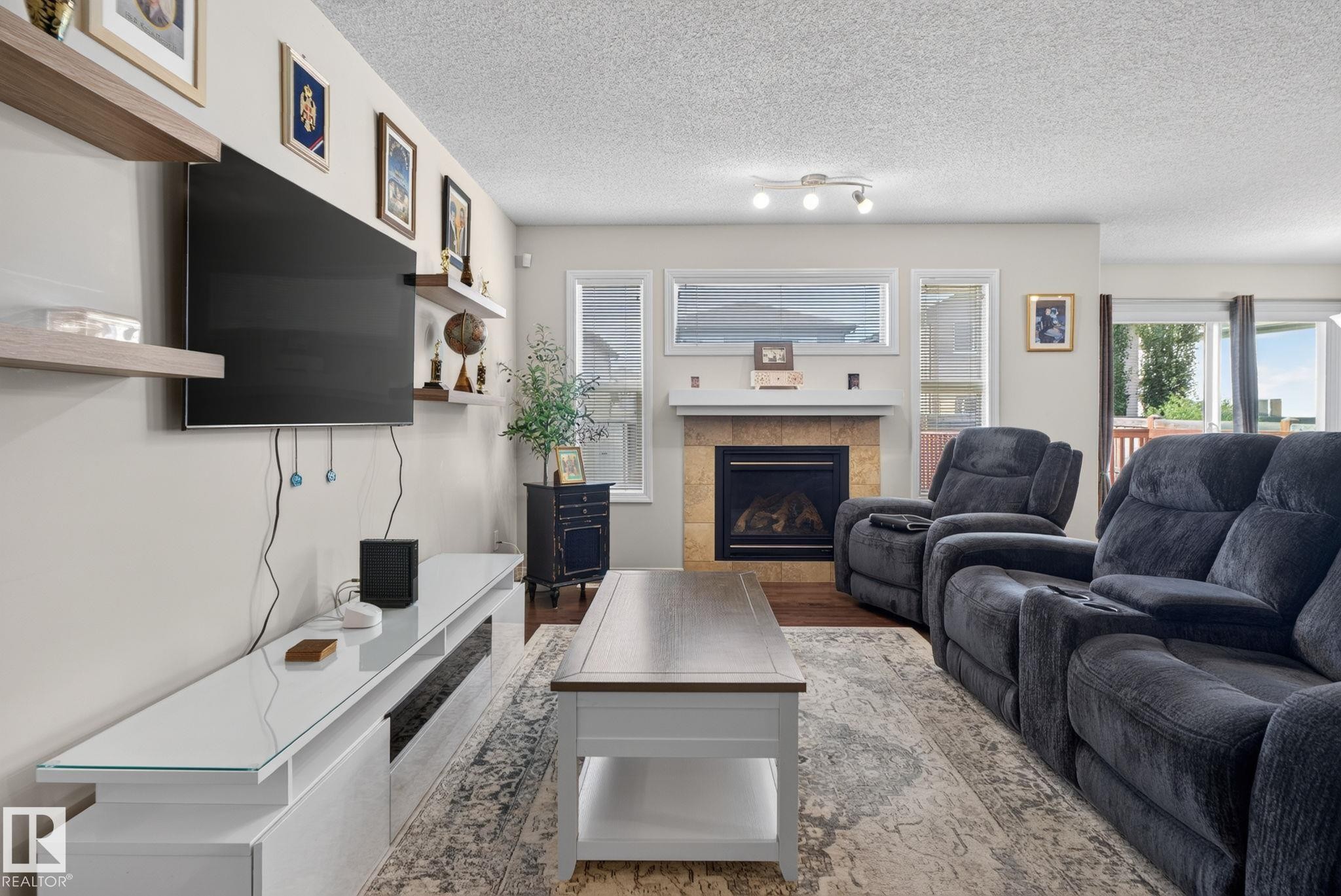 Living area featuring wood-finish flooring, a tile-surround fireplace with a mantel, and multiple windows providing natural light - 7858 170A Avenue, Edmonton, AB