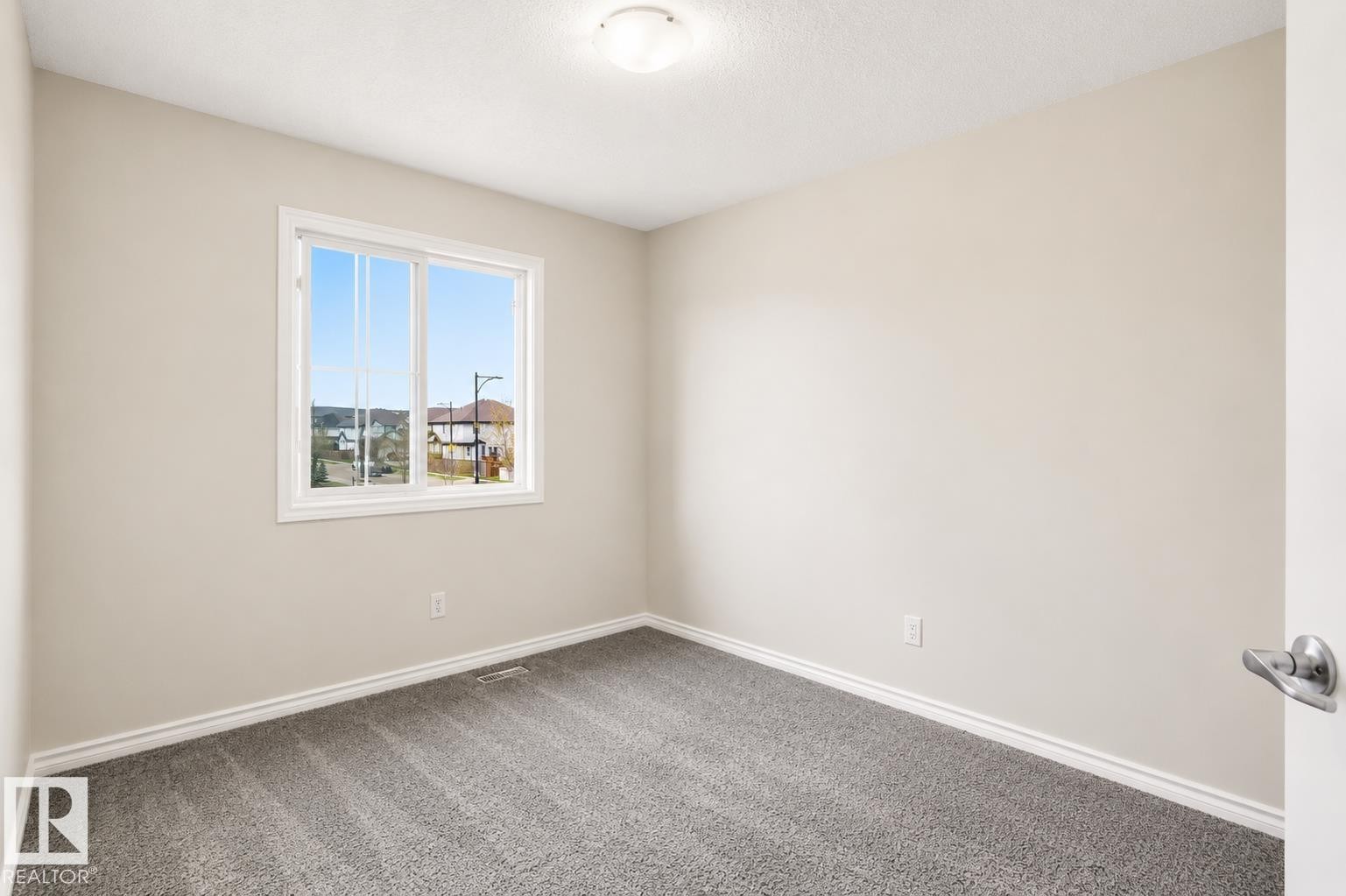 Bright interior room featuring a window with a white frame, light neutral wall paint, gray carpeting, and white baseboards - 445 Watt Boulevard Sw, Edmonton, AB - Indoor Photo Showing Other Room