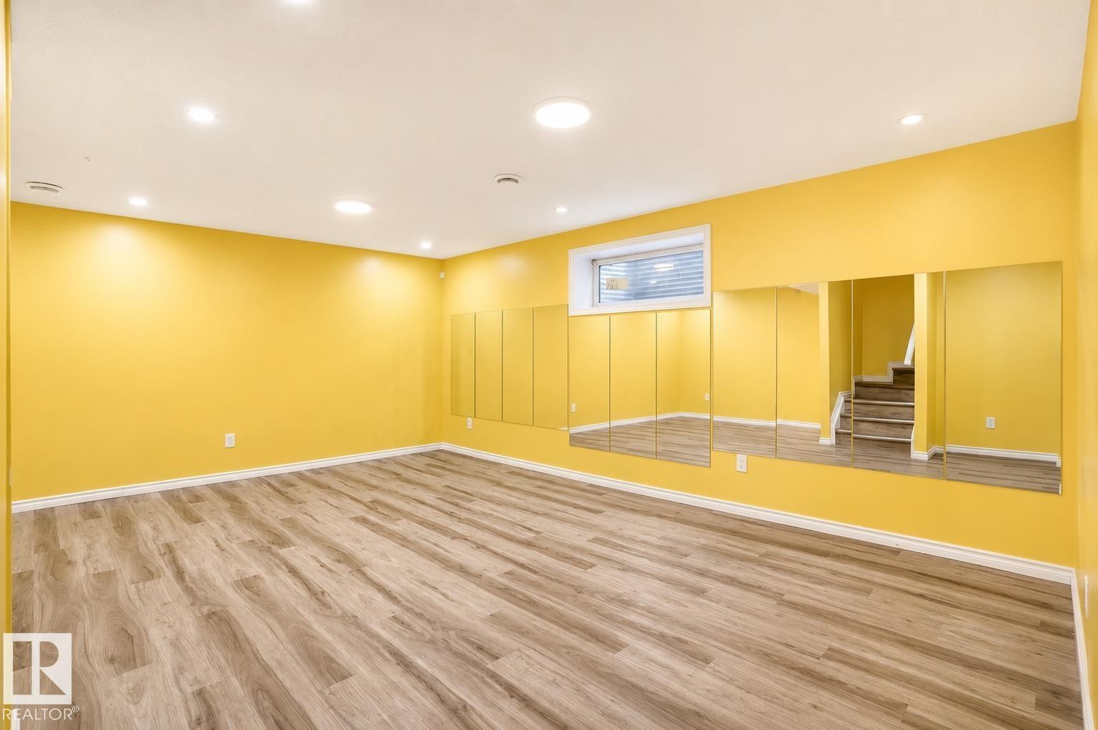 Spacious lower-level room featuring light wood-finish flooring, recessed ceiling lighting, a horizontal window with blinds, and a mirrored wall panel - 445 Watt Boulevard Sw, Edmonton, AB - Indoor Photo Showing Other Room