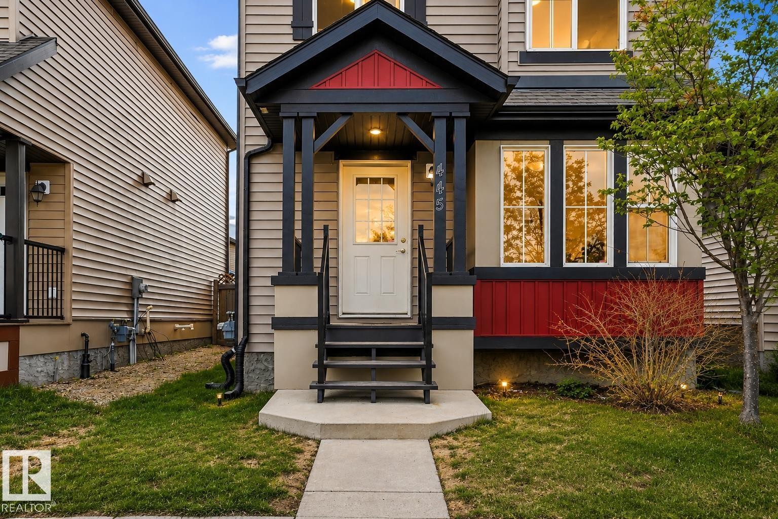 Front exterior featuring a covered entry porch, dark trim accents, warm red paneling, and a mature tree - 445 Watt Boulevard Sw, Edmonton, AB - Outdoor