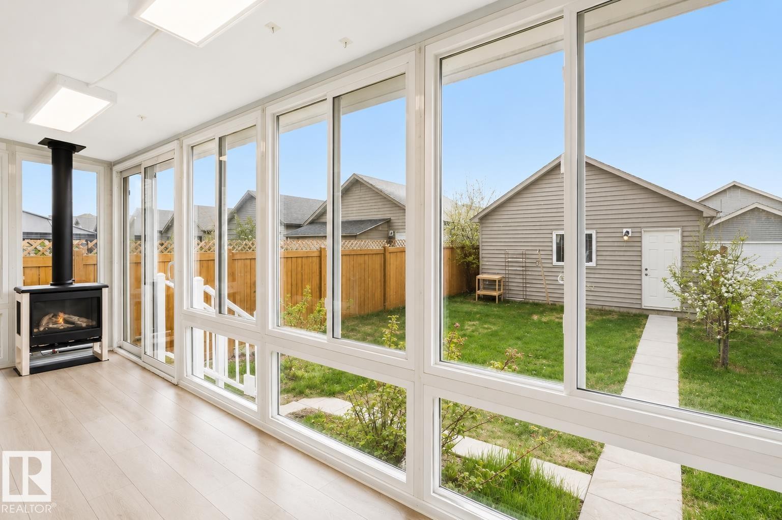 Sunroom featuring a freestanding fireplace, light wood-finish flooring, and expansive windows - 445 Watt Boulevard Sw, Edmonton, AB - Indoor With Fireplace