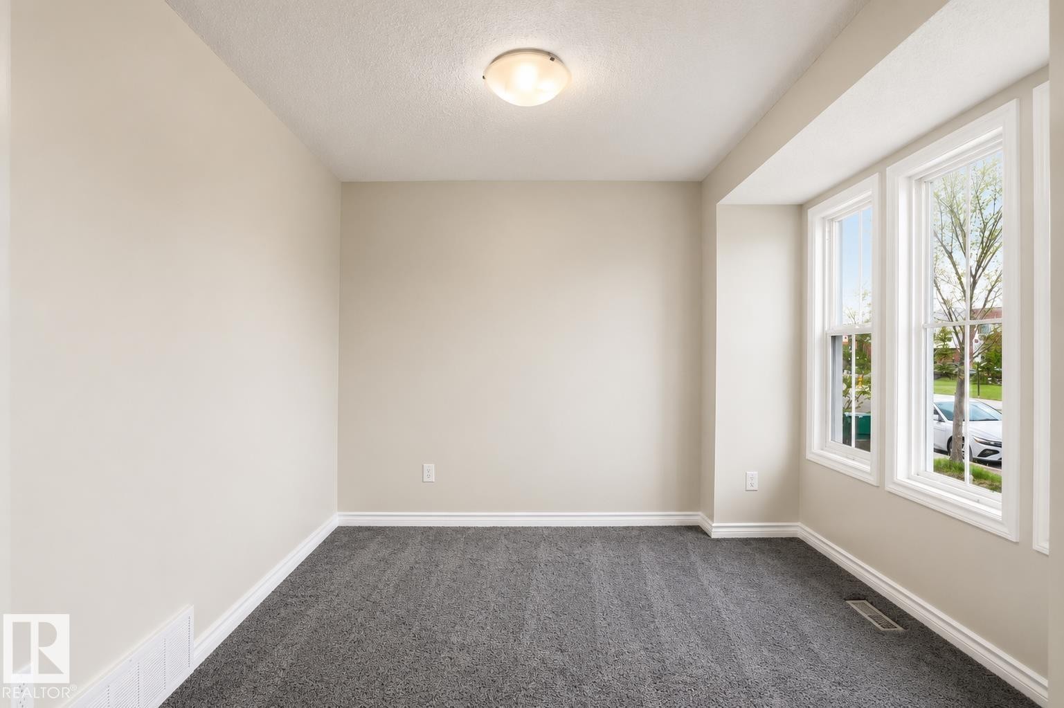 Neutral-toned room featuring a large triple window, textured gray carpeting, a ceiling-mounted light fixture, and white baseboards - 445 Watt Boulevard Sw, Edmonton, AB - Indoor Photo Showing Other Room