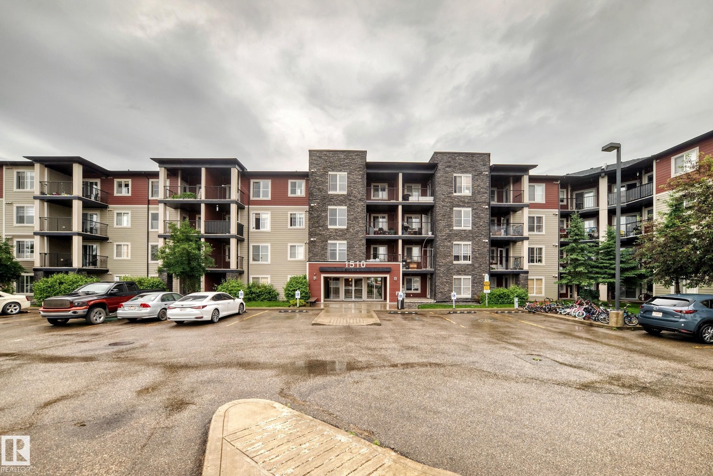 Multi-story residential building featuring a stone and stucco facade, private balconies, and a designated parking area - #417 1510 Watt Dr Sw, Edmonton, AB - Outdoor With Balcony With Facade
