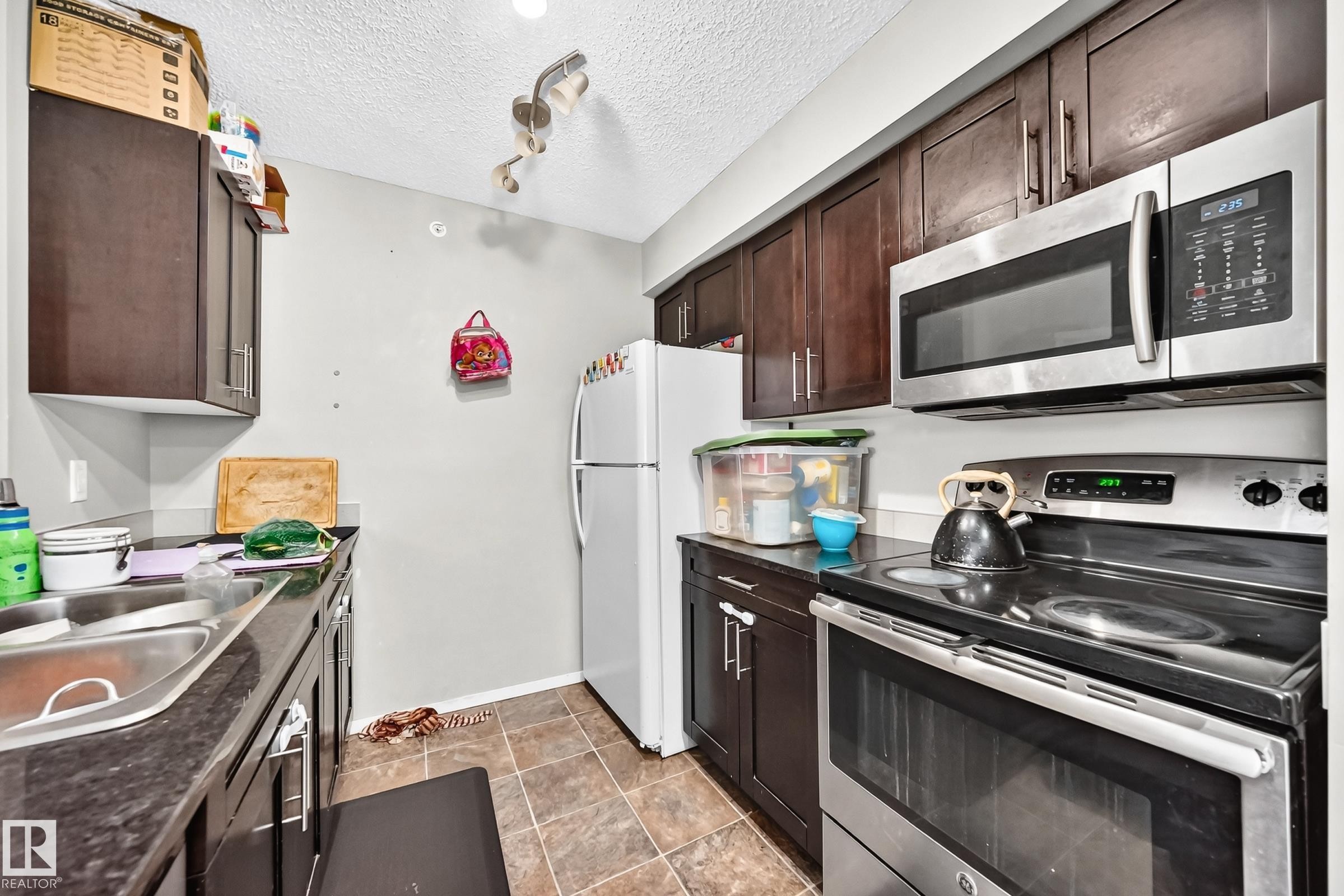 Kitchen featuring dark wood cabinetry, a stainless steel over-the-range microwave, and a stainless steel electric range - #417 1510 Watt Dr Sw, Edmonton, AB - Indoor Photo Showing Kitchen With Double Sink