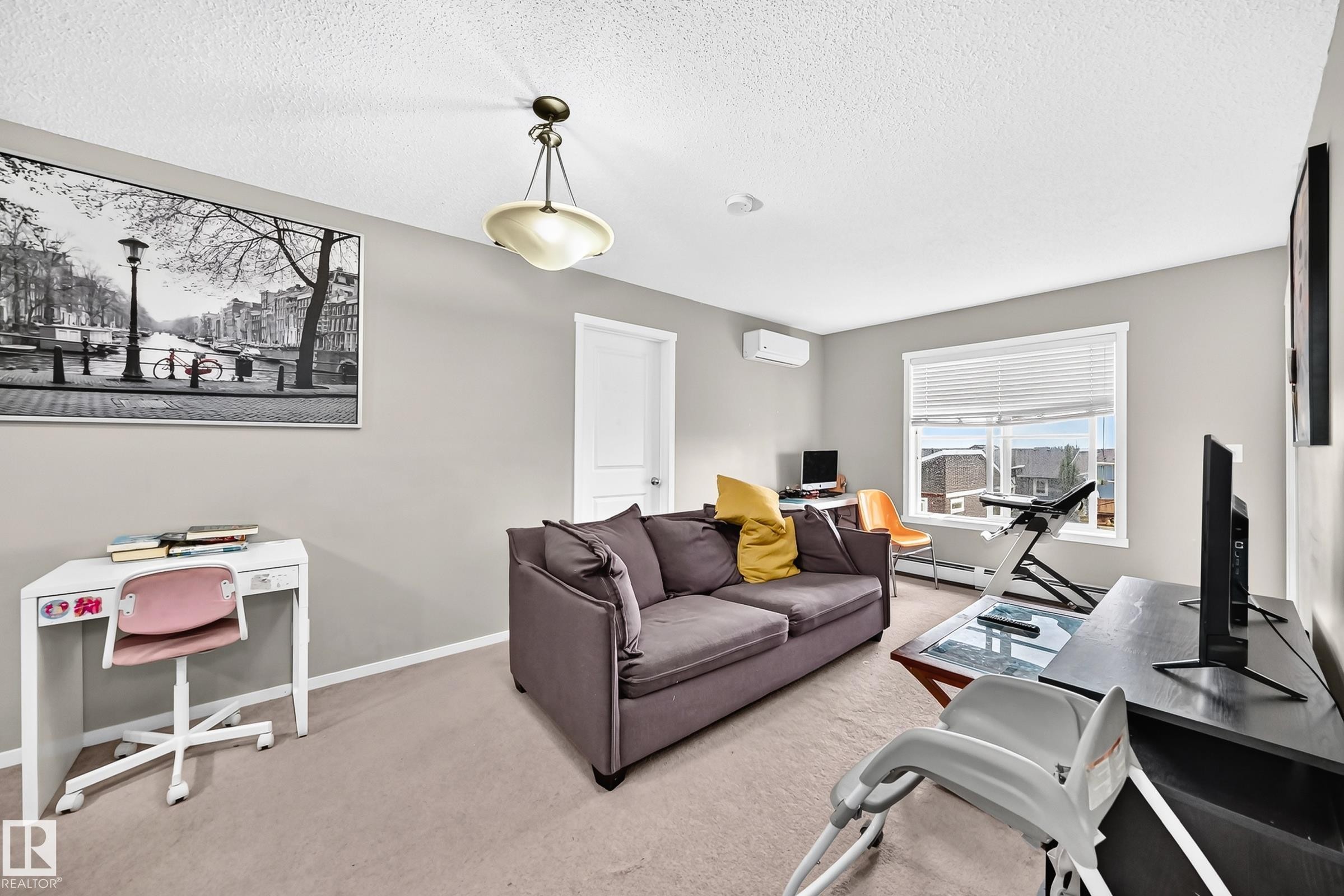 Spacious room featuring neutral carpeting, a large window with horizontal blinds, and a built-in air conditioning unit - #417 1510 Watt Dr Sw, Edmonton, AB - Indoor Photo Showing Living Room