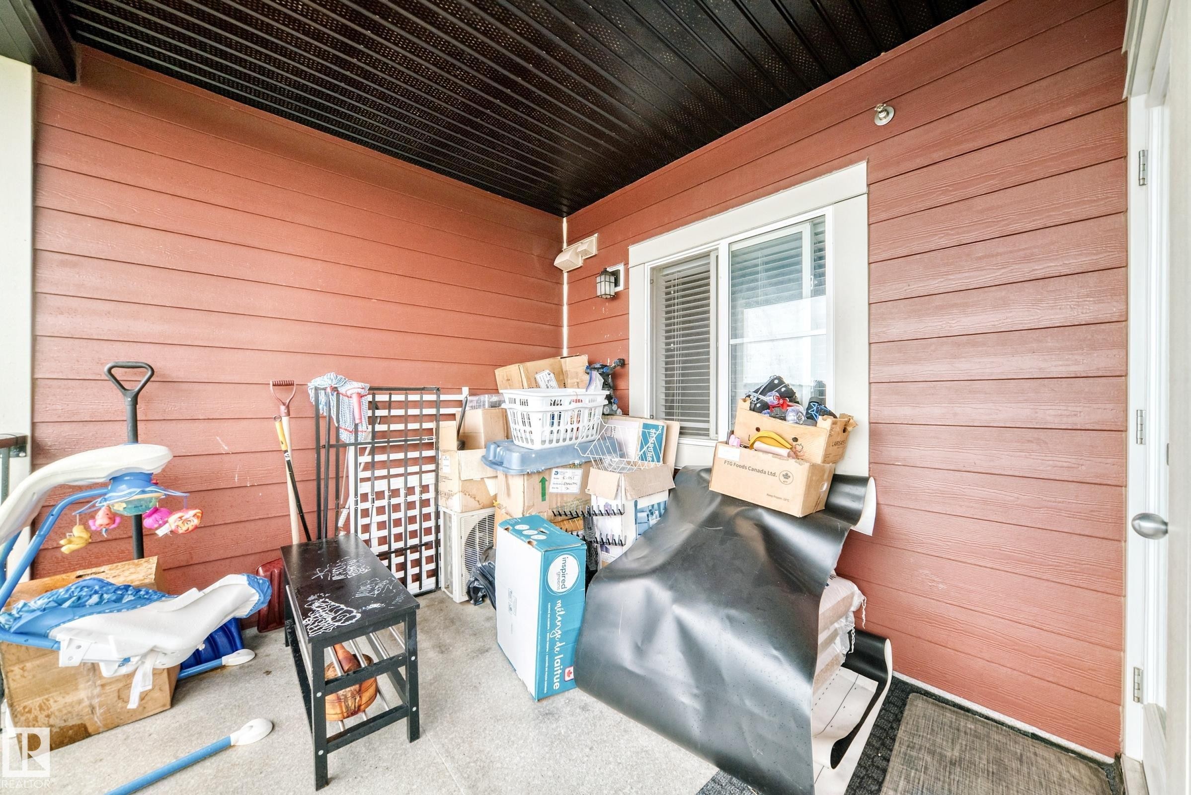 Covered patio space featuring an overhead soffit, red plank siding, and a white-framed window - #417 1510 Watt Dr Sw, Edmonton, AB - Outdoor With Exterior