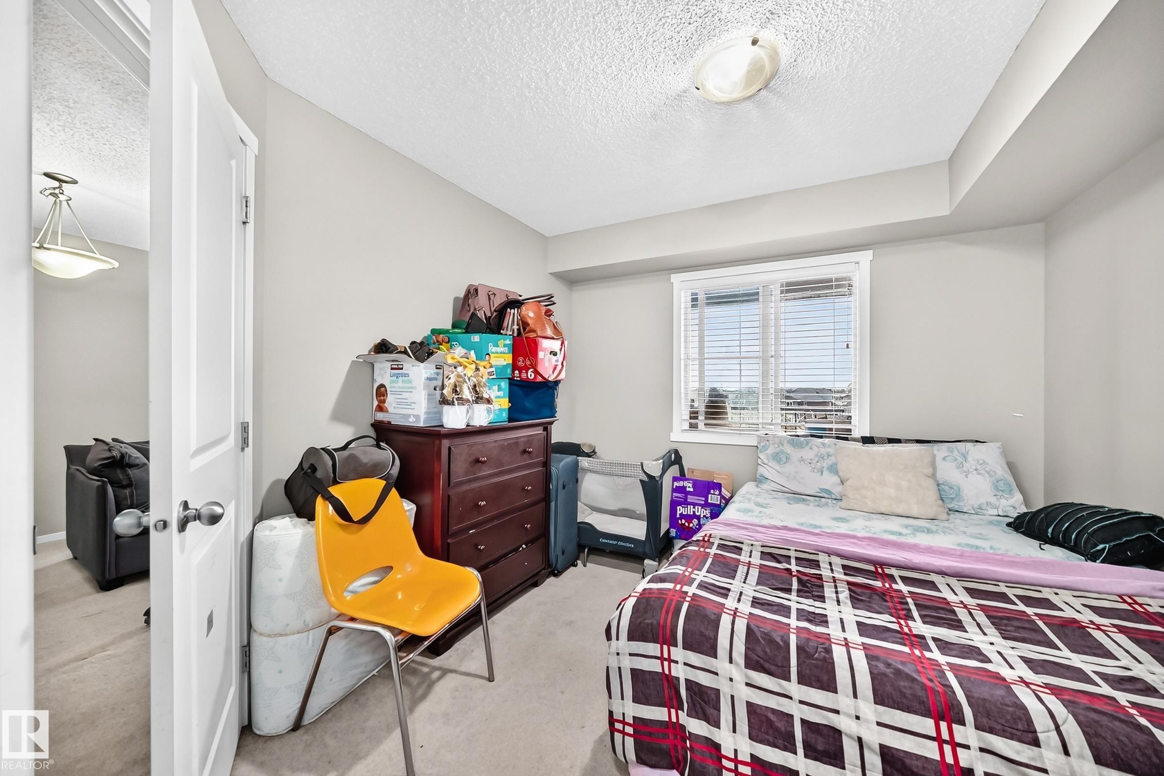 Carpeted bedroom with a window featuring horizontal blinds, neutral wall tones, and a ceiling-mounted light fixture - #417 1510 Watt Dr Sw, Edmonton, AB - Indoor Photo Showing Bedroom