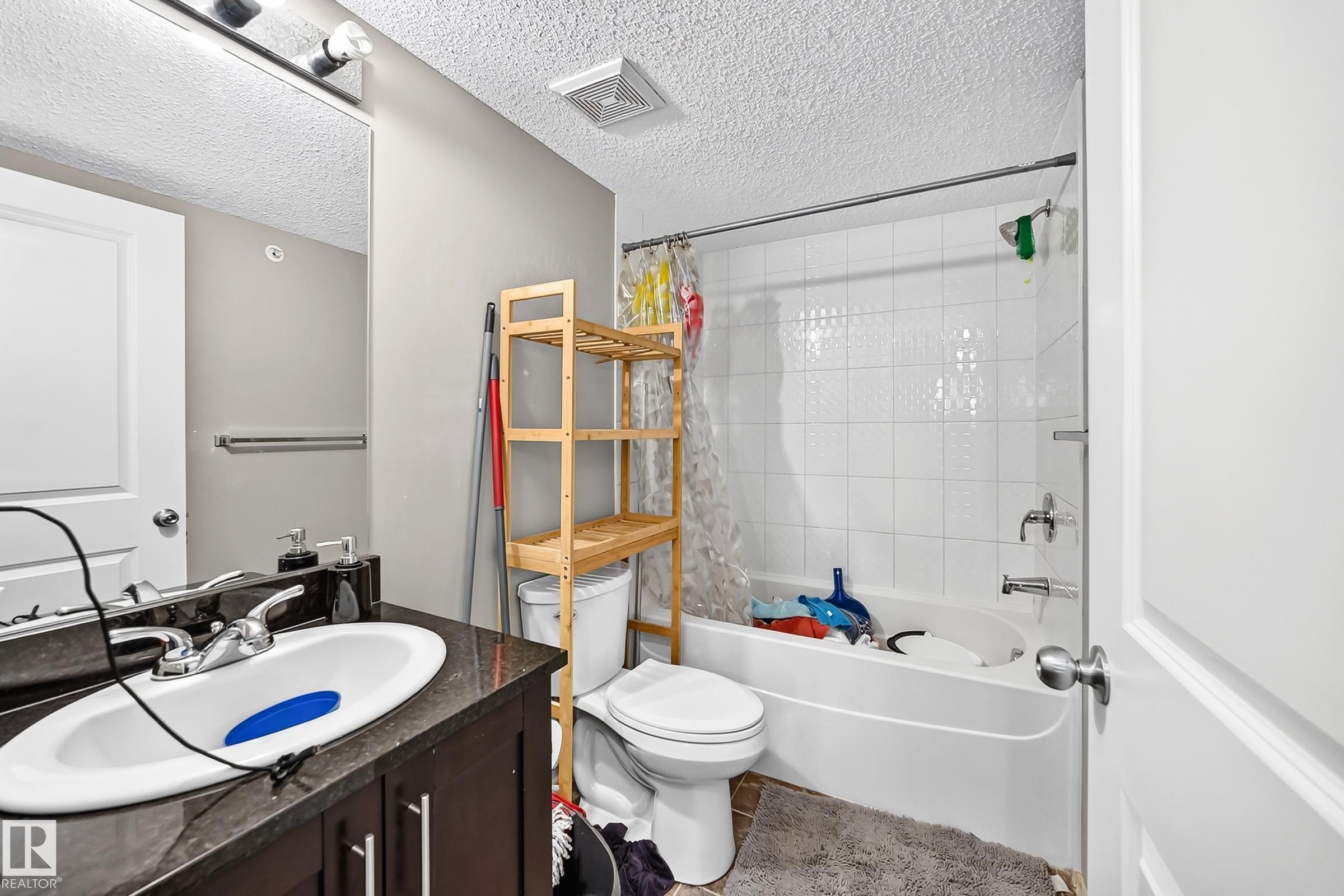 Bathroom featuring a vanity with dark cabinetry and countertop, a white drop-in sink, and a chrome faucet - #417 1510 Watt Dr Sw, Edmonton, AB - Indoor Photo Showing Bathroom