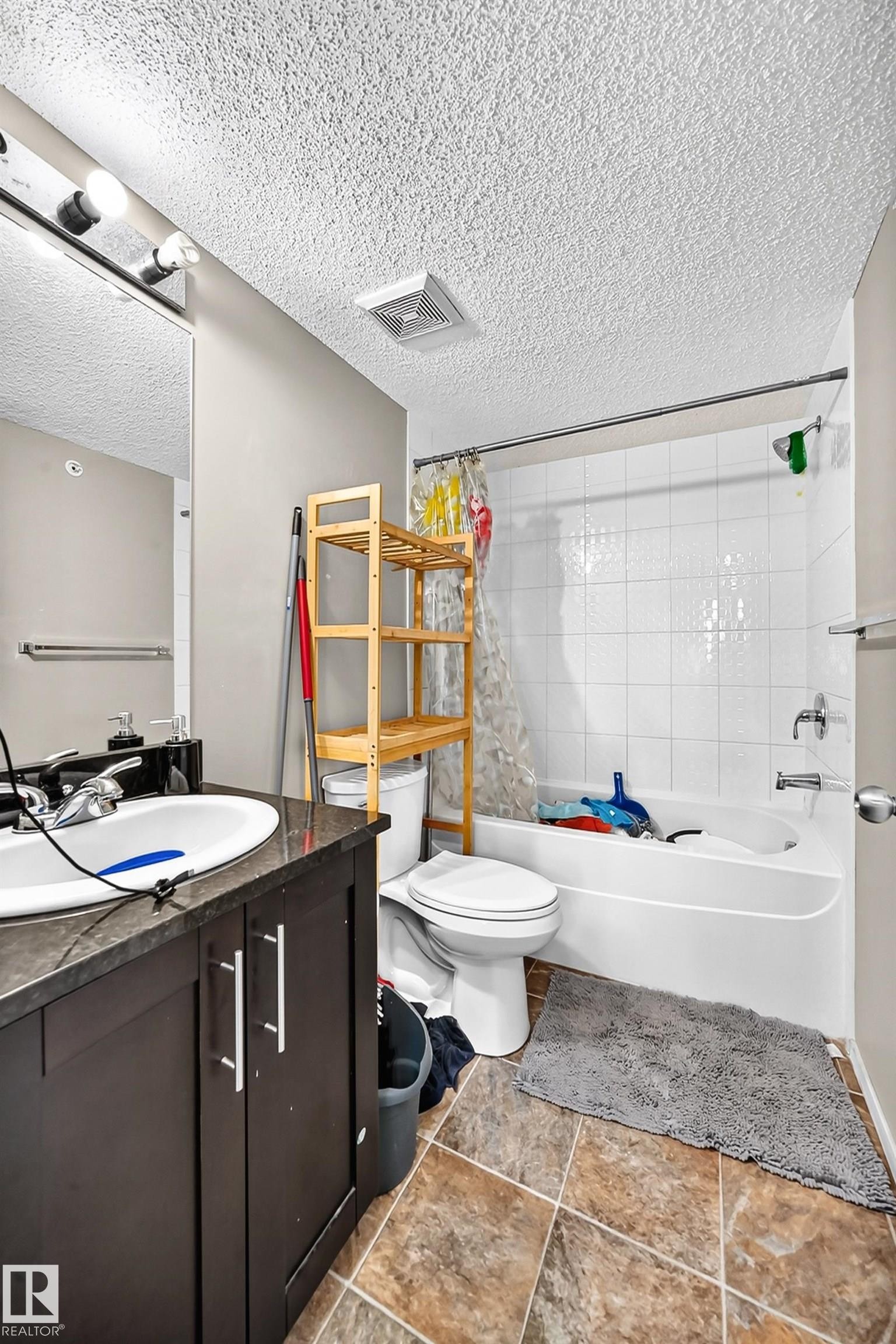 Bathroom featuring a built-in vanity with a dark countertop and white basin, a white toilet, and a white bathtub with subway tile surround - #417 1510 Watt Dr Sw, Edmonton, AB - Indoor Photo Showing Bathroom