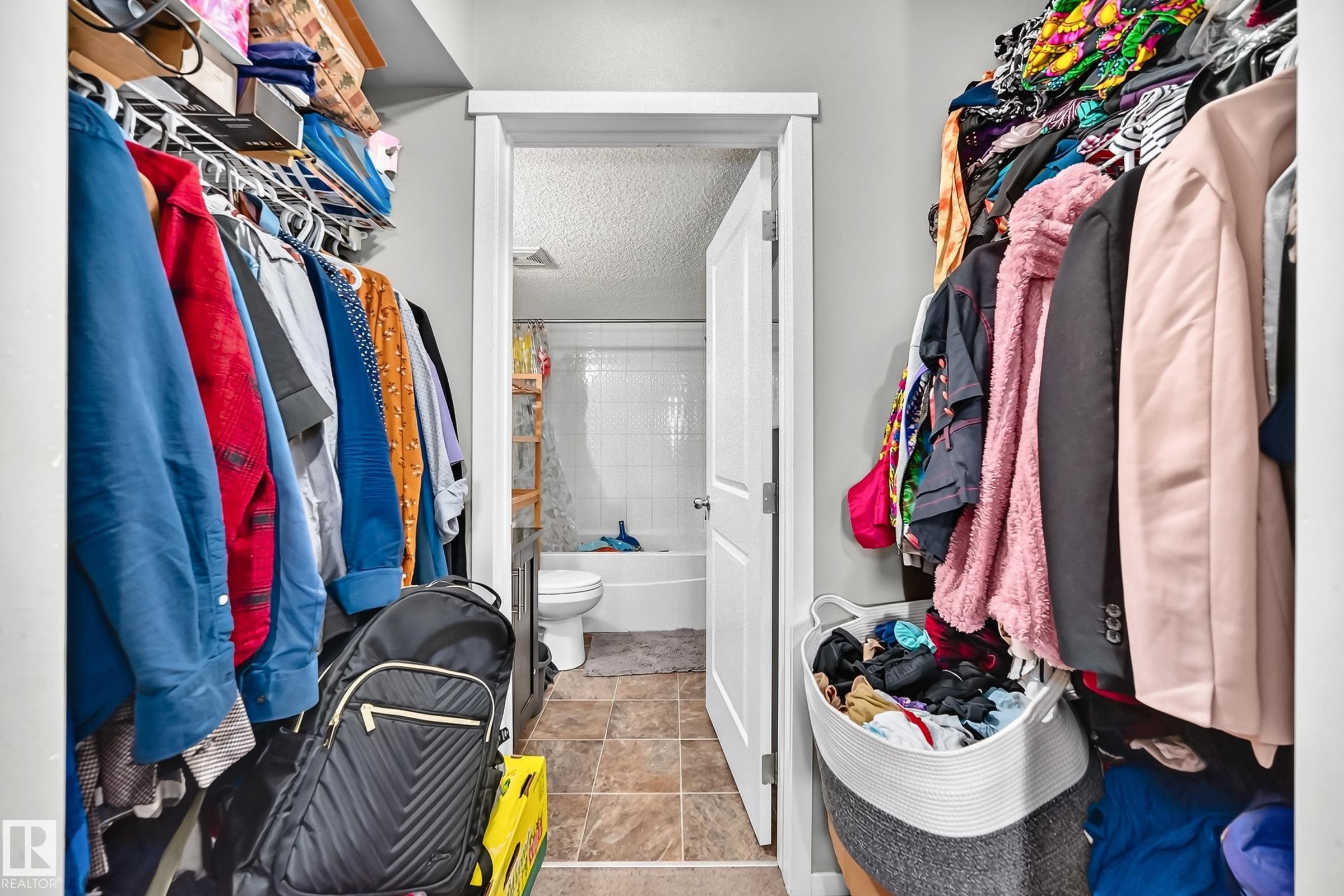 Walk-in closet featuring wire shelving, hanging rods, and an entryway to a full bathroom with a white tub and tiled walls - #417 1510 Watt Dr Sw, Edmonton, AB - Indoor With Storage
