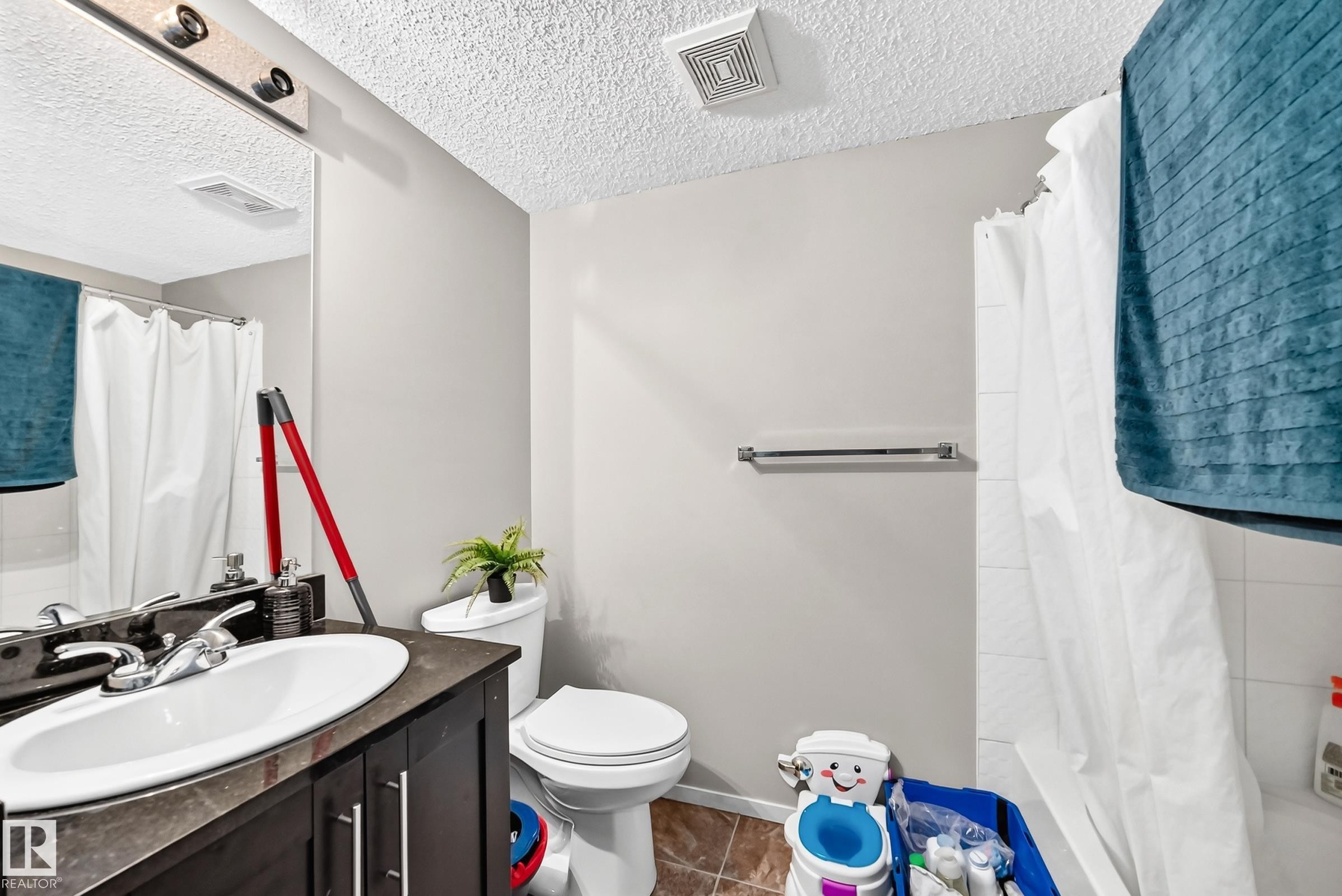Bathroom featuring a vanity with an integrated sink, dark wood-finish cabinetry, a toilet, a shower with white subway tile, and a textured ceiling - #417 1510 Watt Dr Sw, Edmonton, AB - Indoor Photo Showing Bathroom