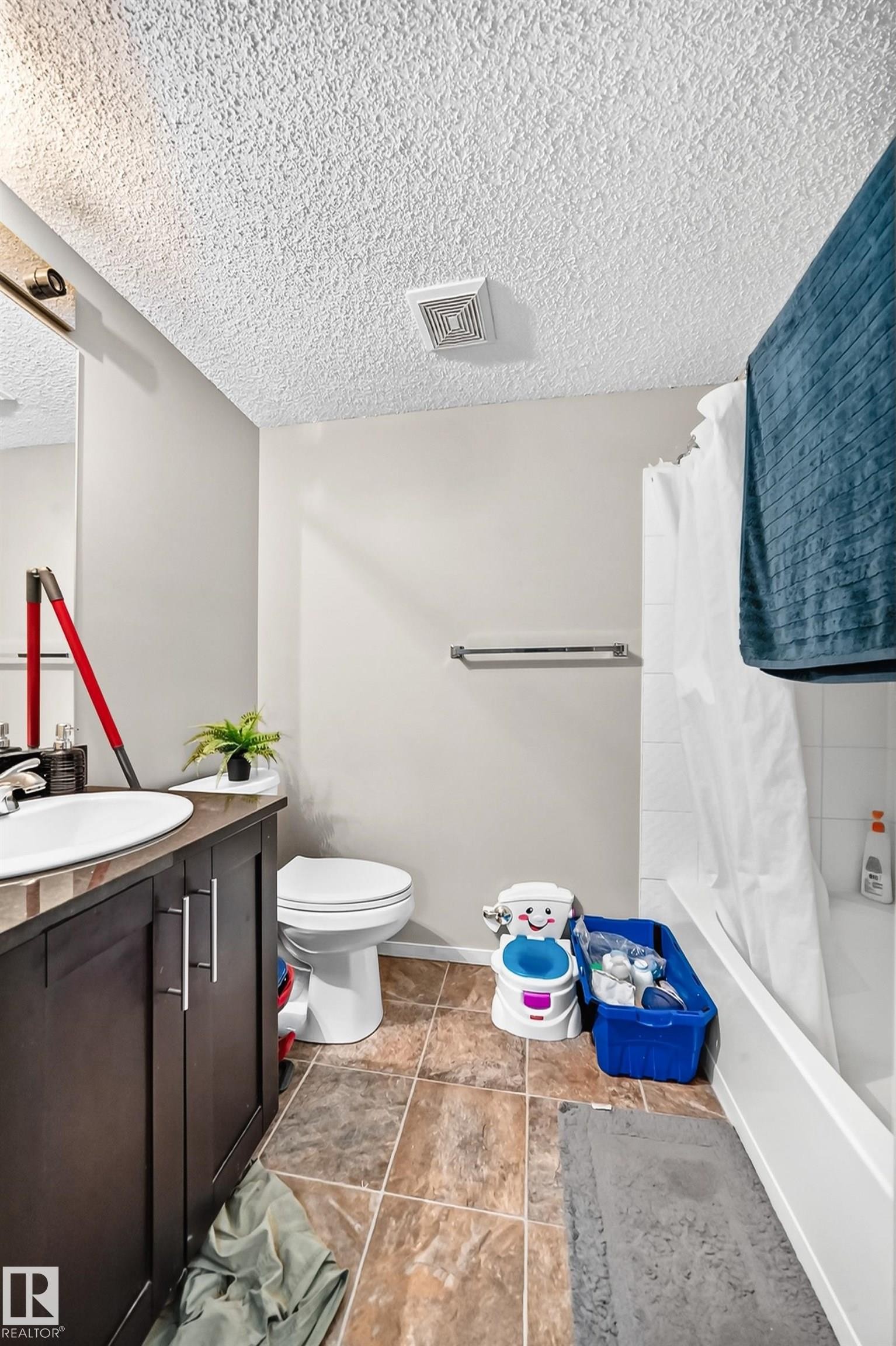 Bathroom featuring a dark wood-finish vanity with an undermount sink, a toilet, an integrated bathtub and shower with white subway tile surround, and square tile flooring - #417 1510 Watt Dr Sw, Edmonton, AB - Indoor Photo Showing Bathroom