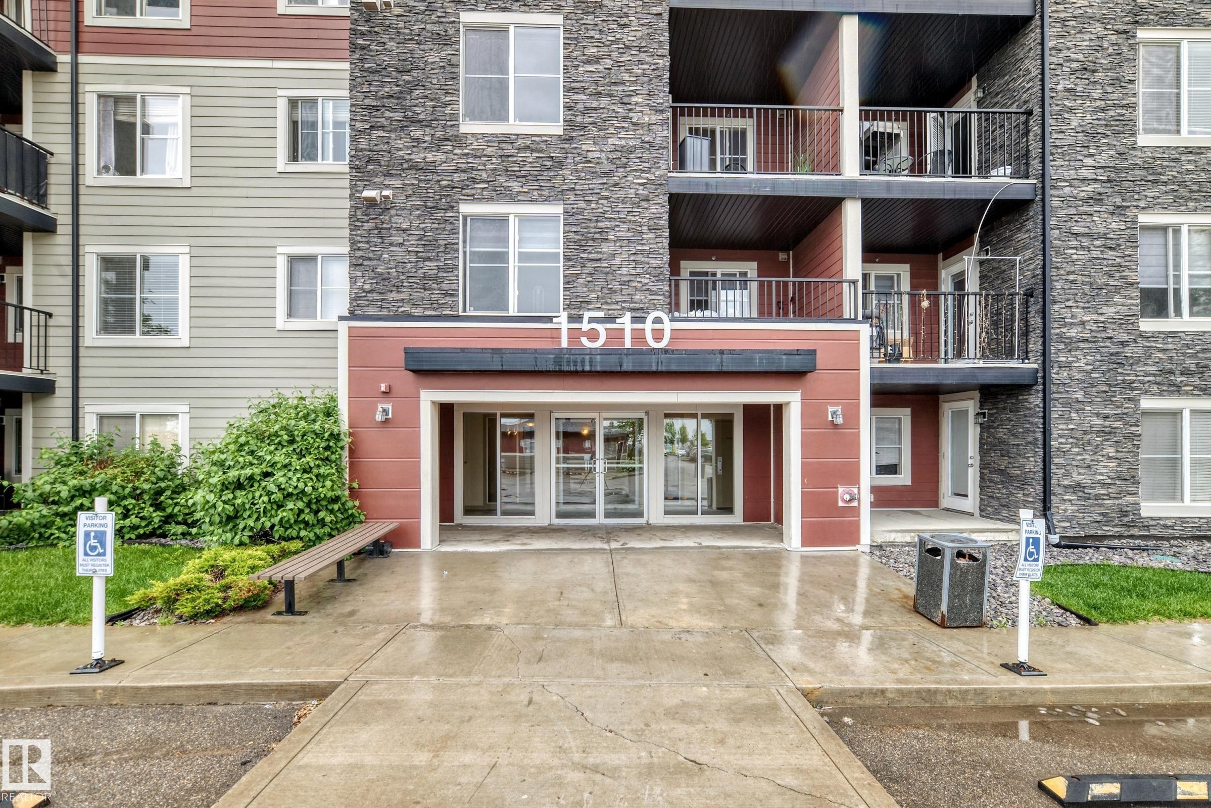 Building entrance featuring stacked stone and horizontal siding, with a covered entryway and glass double doors - #417 1510 Watt Dr Sw, Edmonton, AB - Outdoor With Balcony