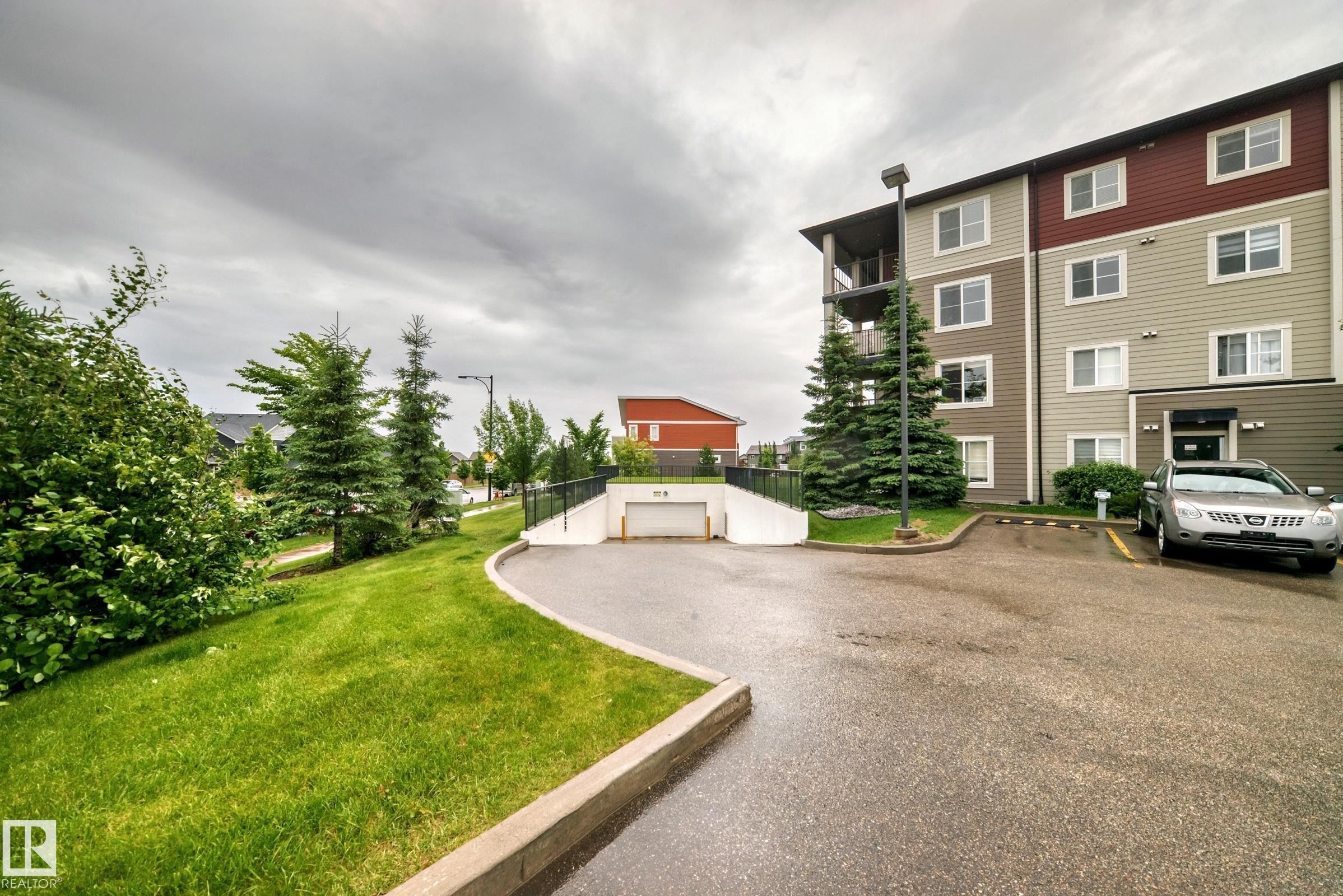 Multi-story residential building with a two-tone exterior, featuring a private balcony, surface parking, and an underground parking entrance - #417 1510 Watt Dr Sw, Edmonton, AB - Outdoor