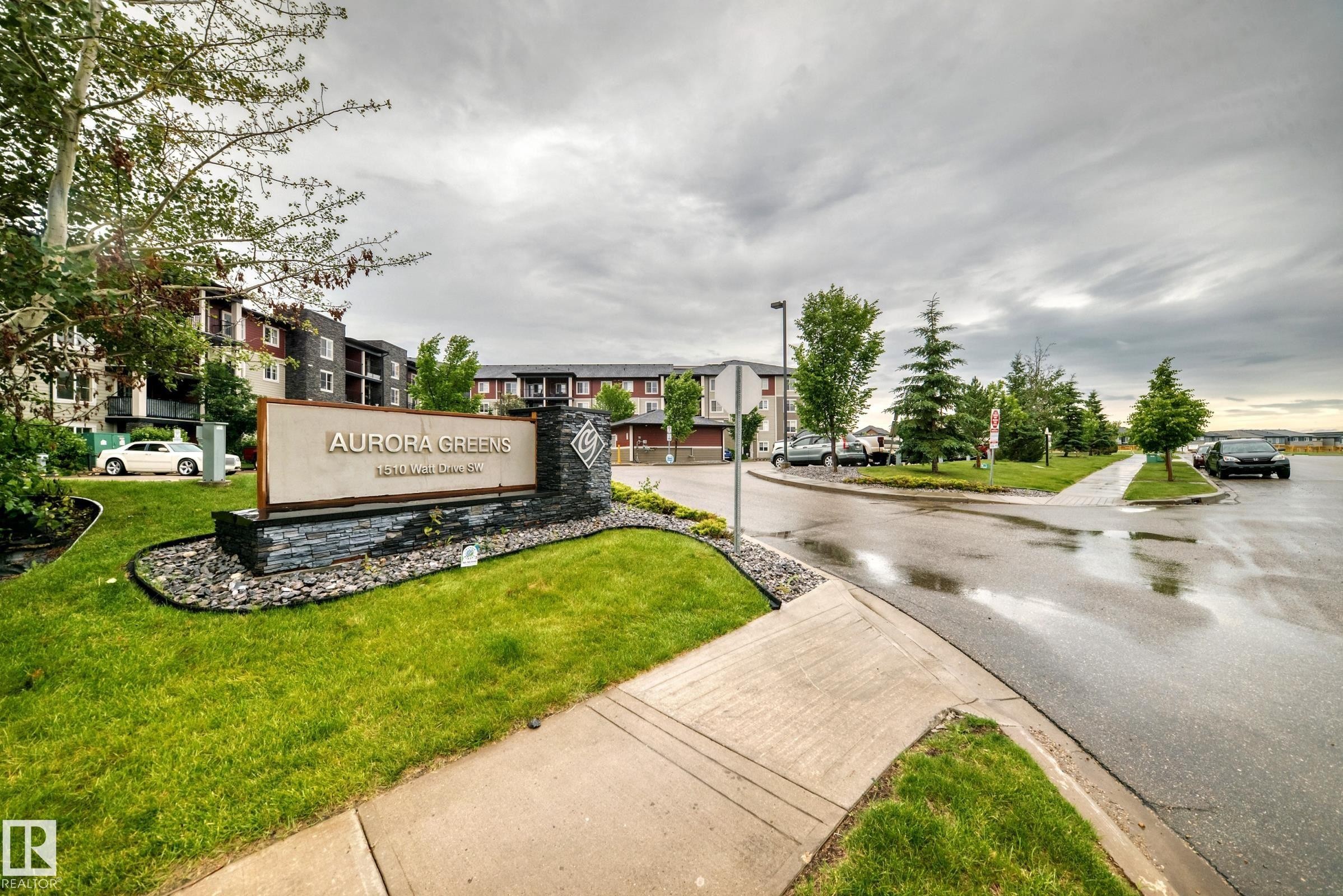 Entry sign for Aurora Greens featuring stone accents and landscaping - #417 1510 Watt Dr Sw, Edmonton, AB - Outdoor With View