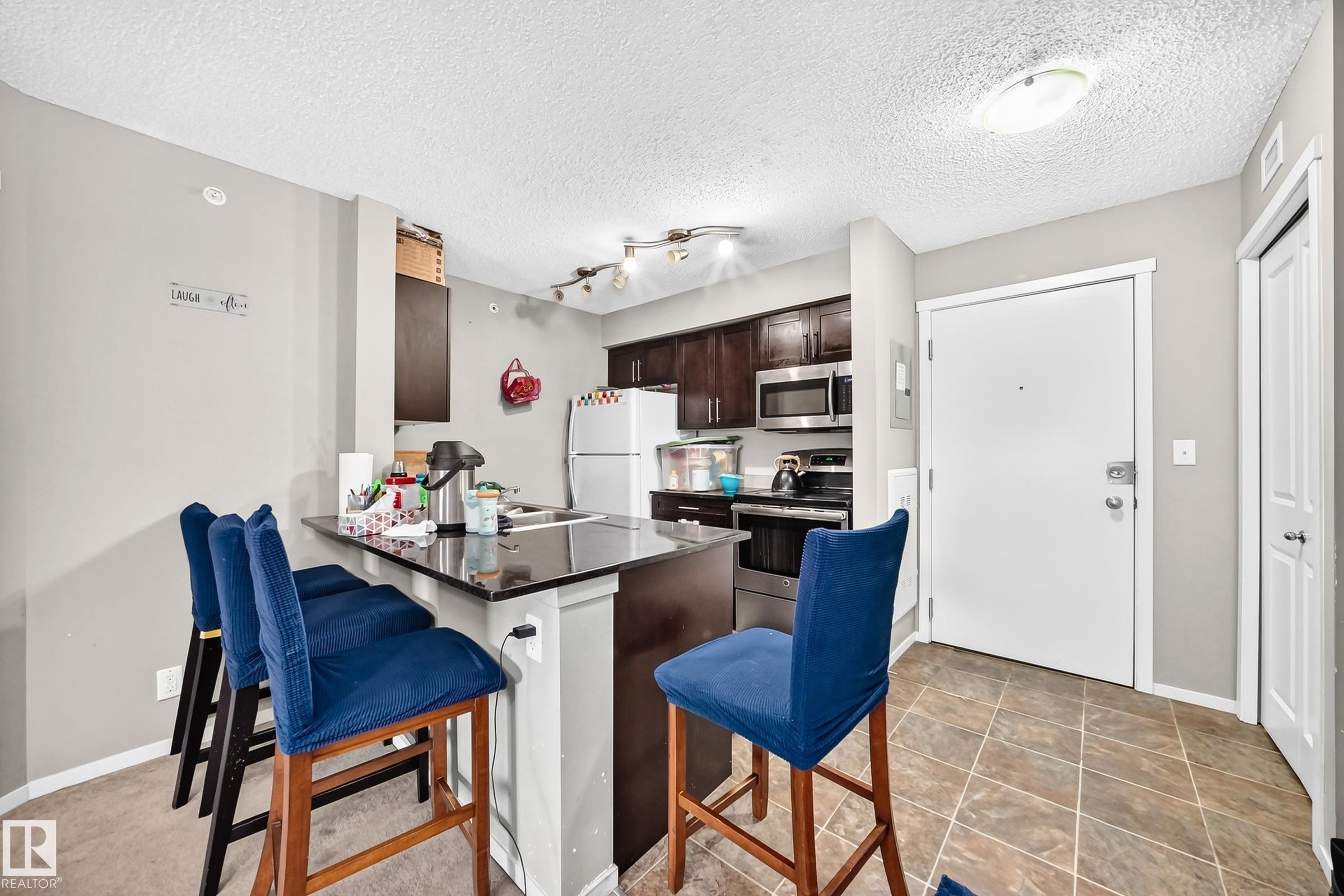 Kitchen featuring dark wood cabinetry, stainless steel appliances, and a breakfast bar with a dark countertop - #417 1510 Watt Dr Sw, Edmonton, AB - Indoor