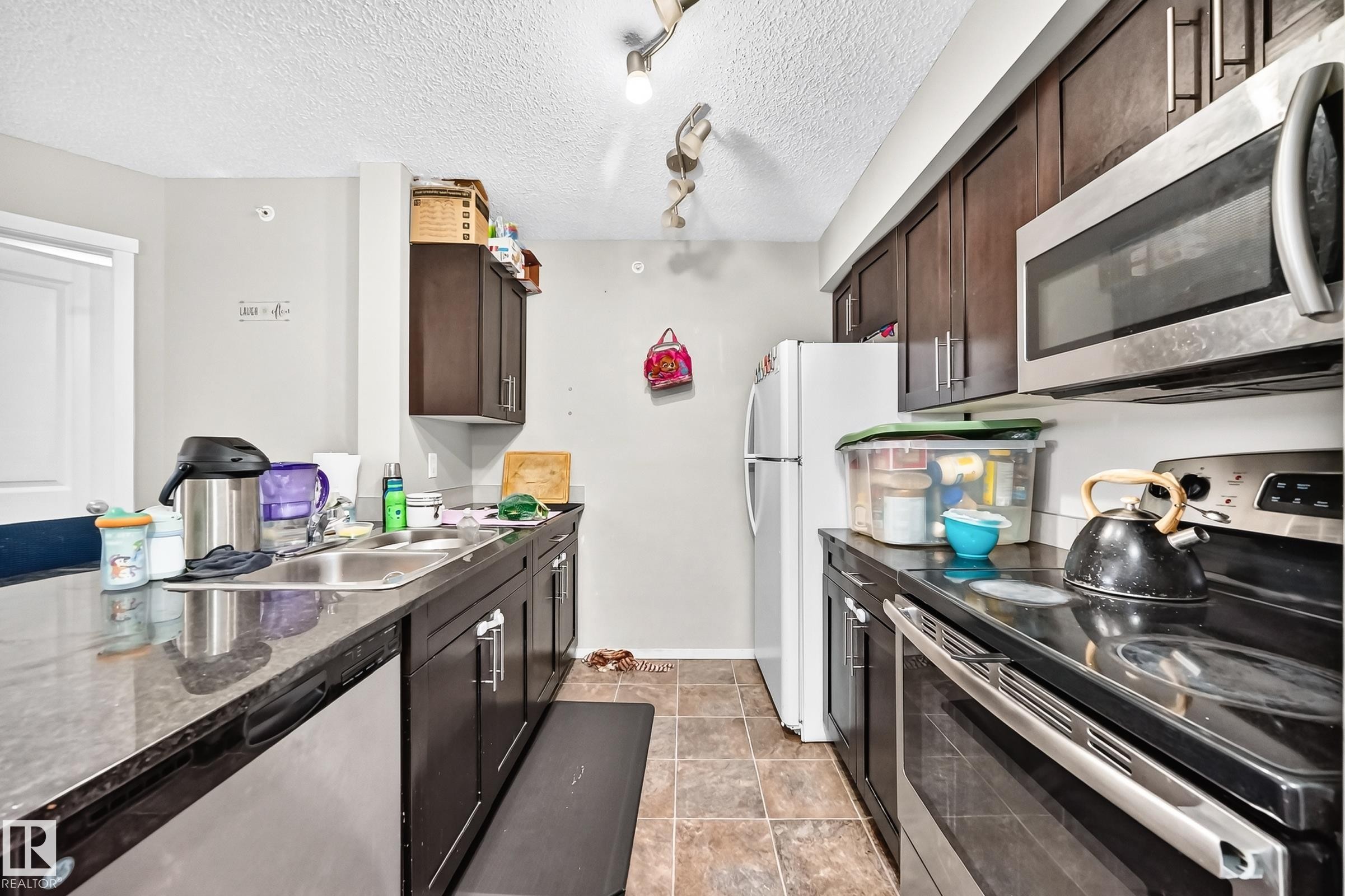 Kitchen featuring dark wood-finish cabinetry, stainless steel appliances, and a double basin sink - #417 1510 Watt Dr Sw, Edmonton, AB - Indoor Photo Showing Kitchen With Double Sink