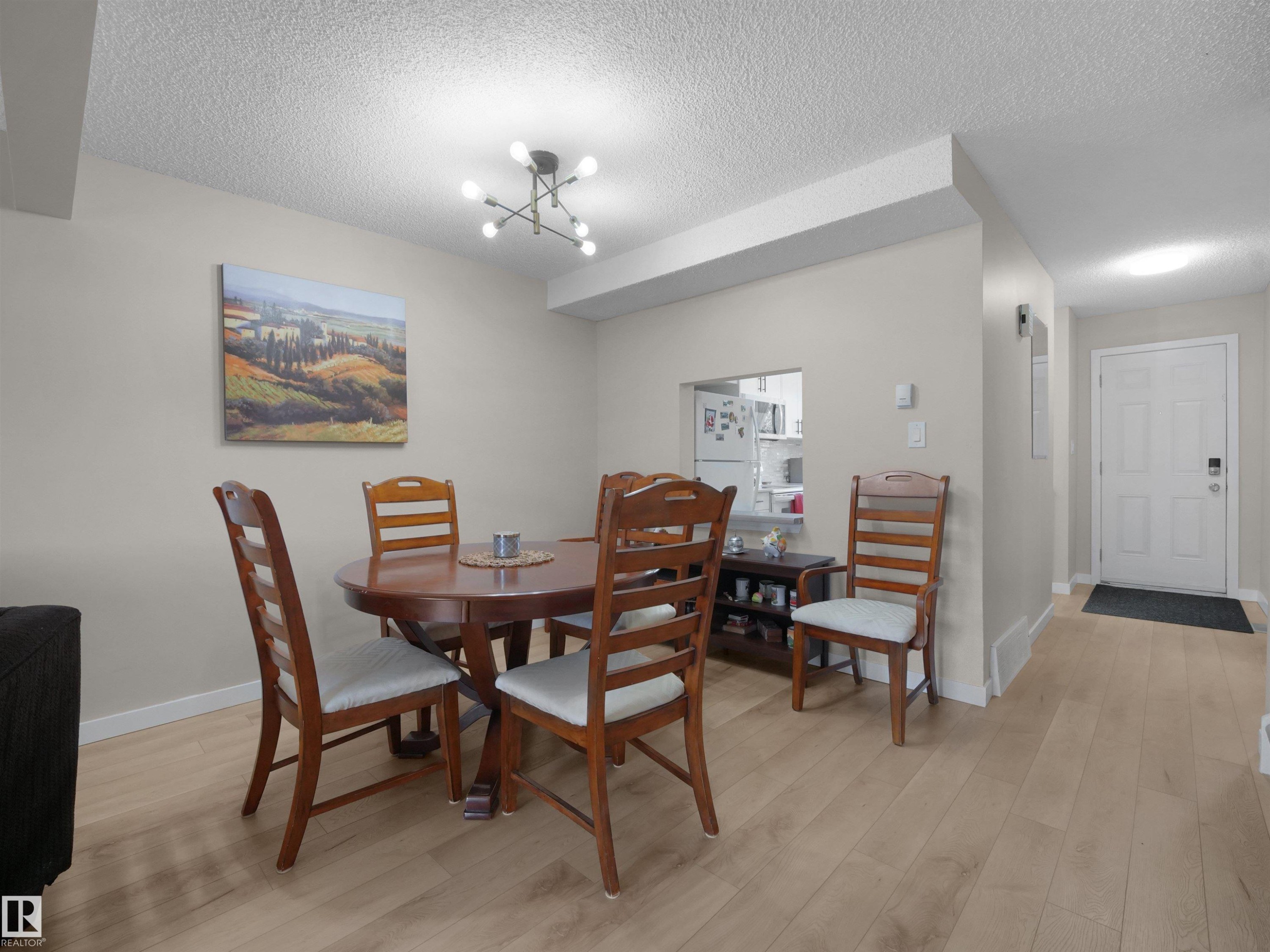 Dining area with wood-finish flooring, a contemporary ceiling light fixture, a pass-through window to the kitchen, and a paneled entry door - 575 Dunluce Road, Edmonton, AB