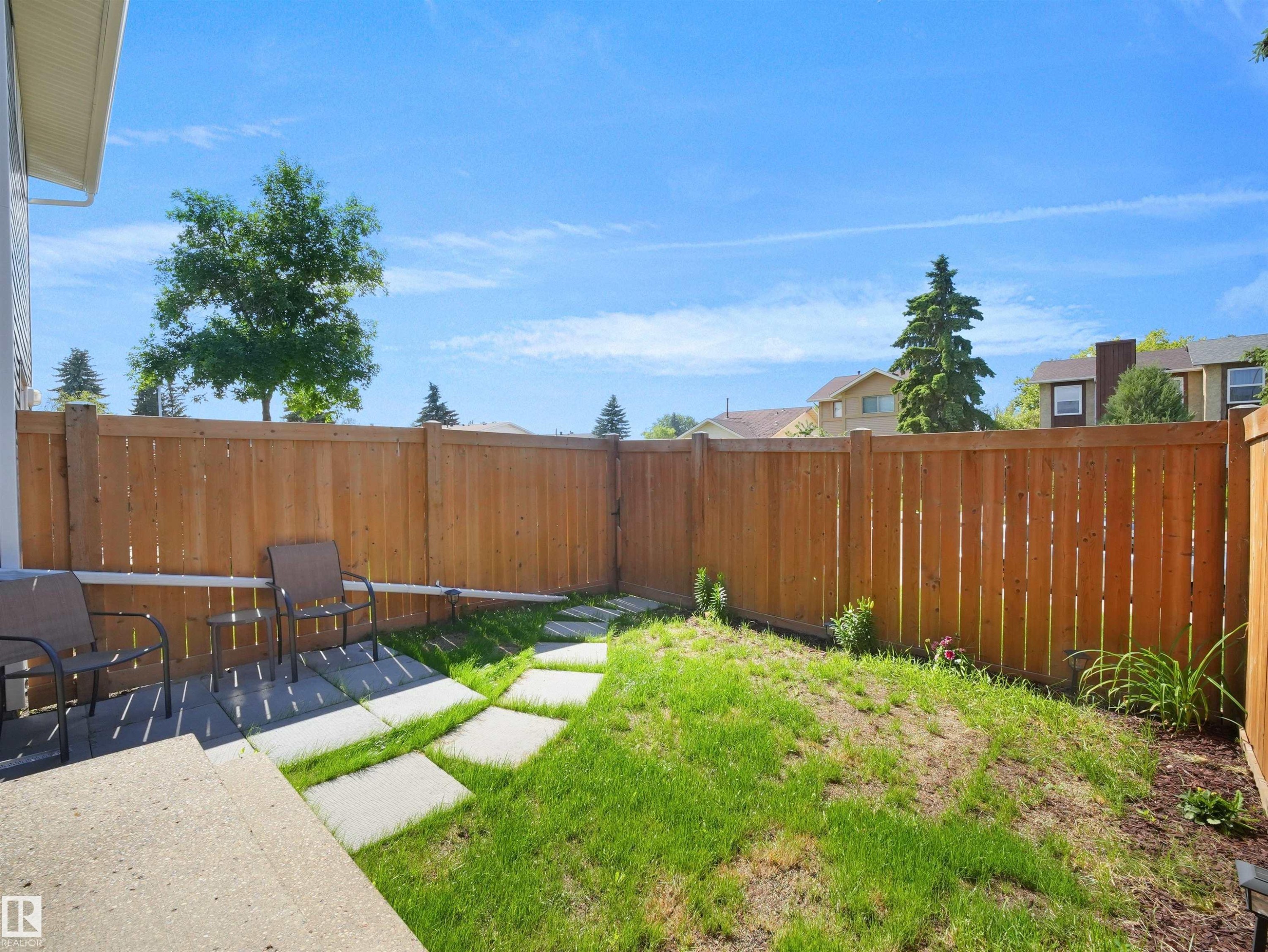 Private backyard featuring a wood fence, concrete patio, and a stepping stone path across the lawn - 575 Dunluce Road, Edmonton, AB