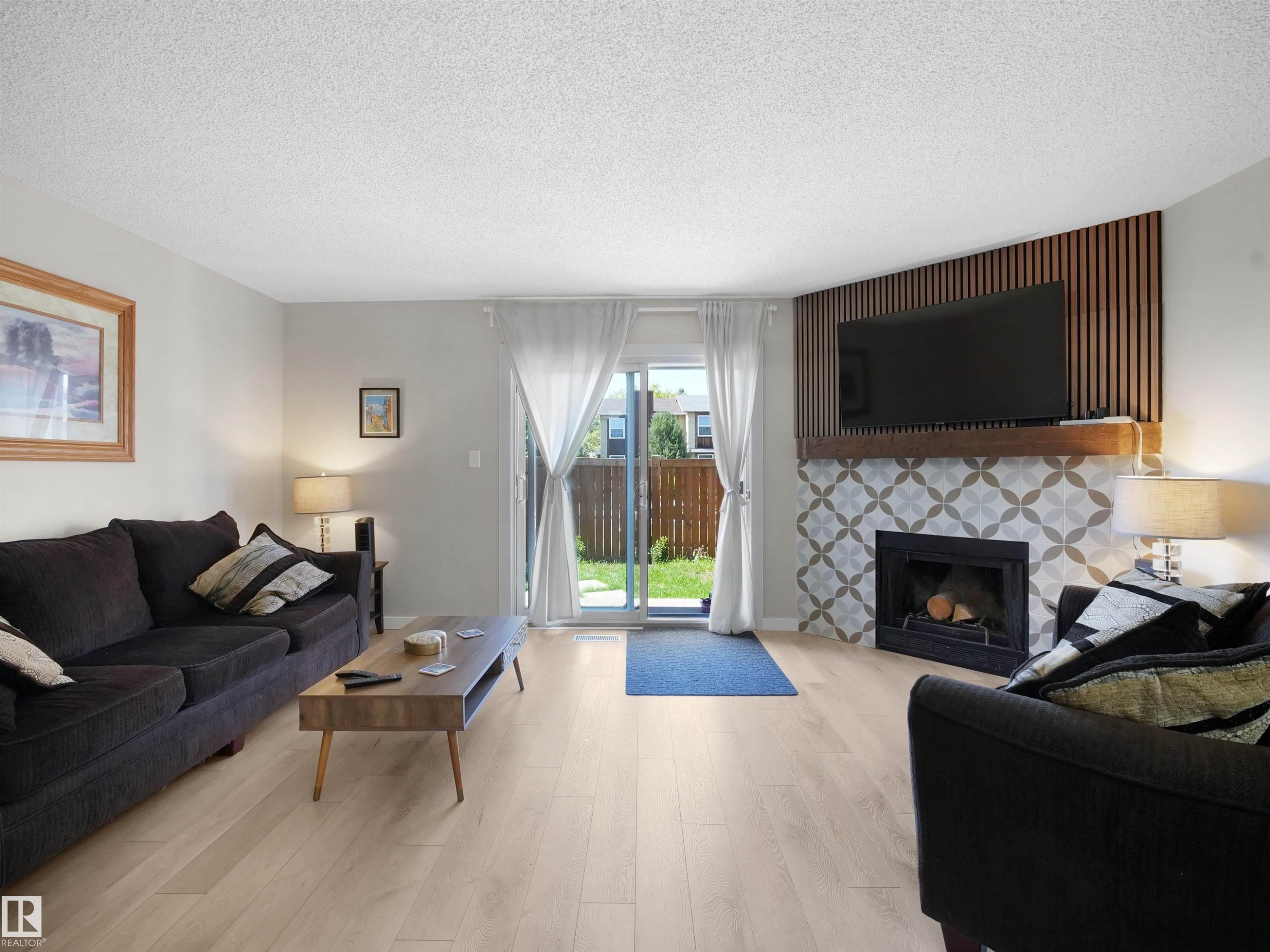 Living area featuring light wood-finish flooring, a decorative fireplace with patterned tile surround, and a wood mantel - 575 Dunluce Road, Edmonton, AB