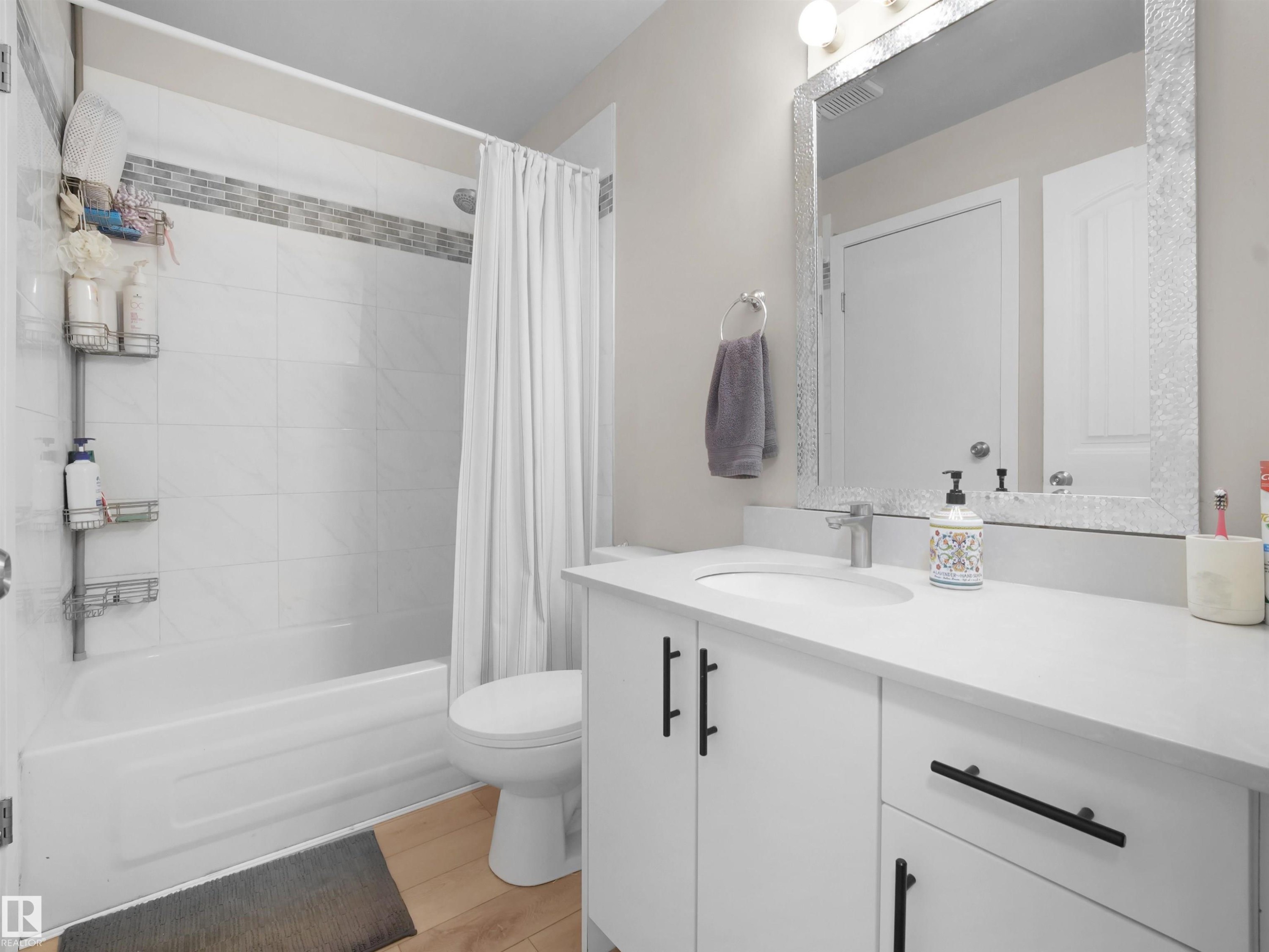 Modern bathroom featuring a white vanity with integrated sink, a large framed mirror, and light wood-finish flooring - 575 Dunluce Road, Edmonton, AB