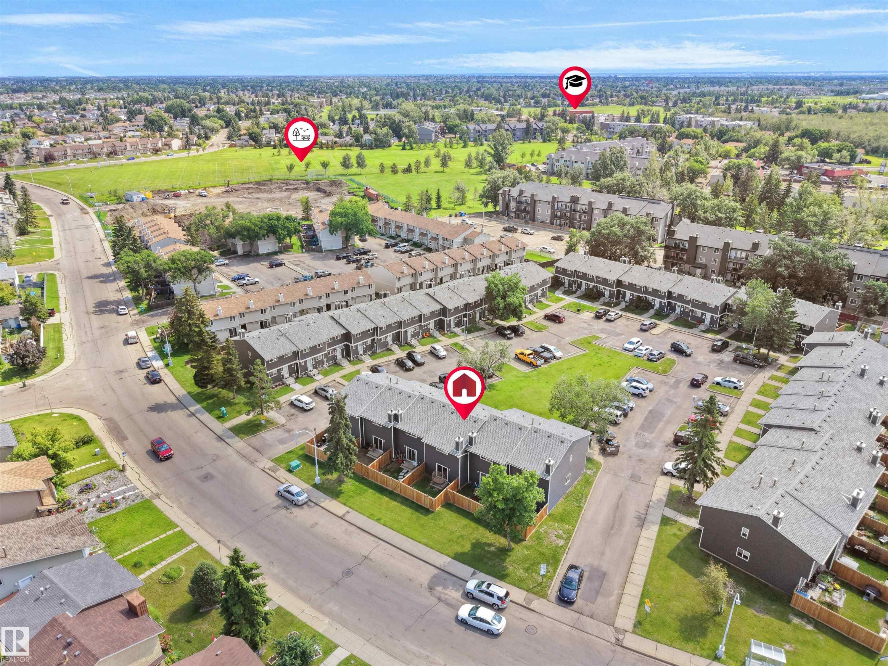 Aerial perspective showcasing a community of townhome-style residences with individual fenced yards, surface parking, and a bordering green space - 575 Dunluce Road, Edmonton, AB